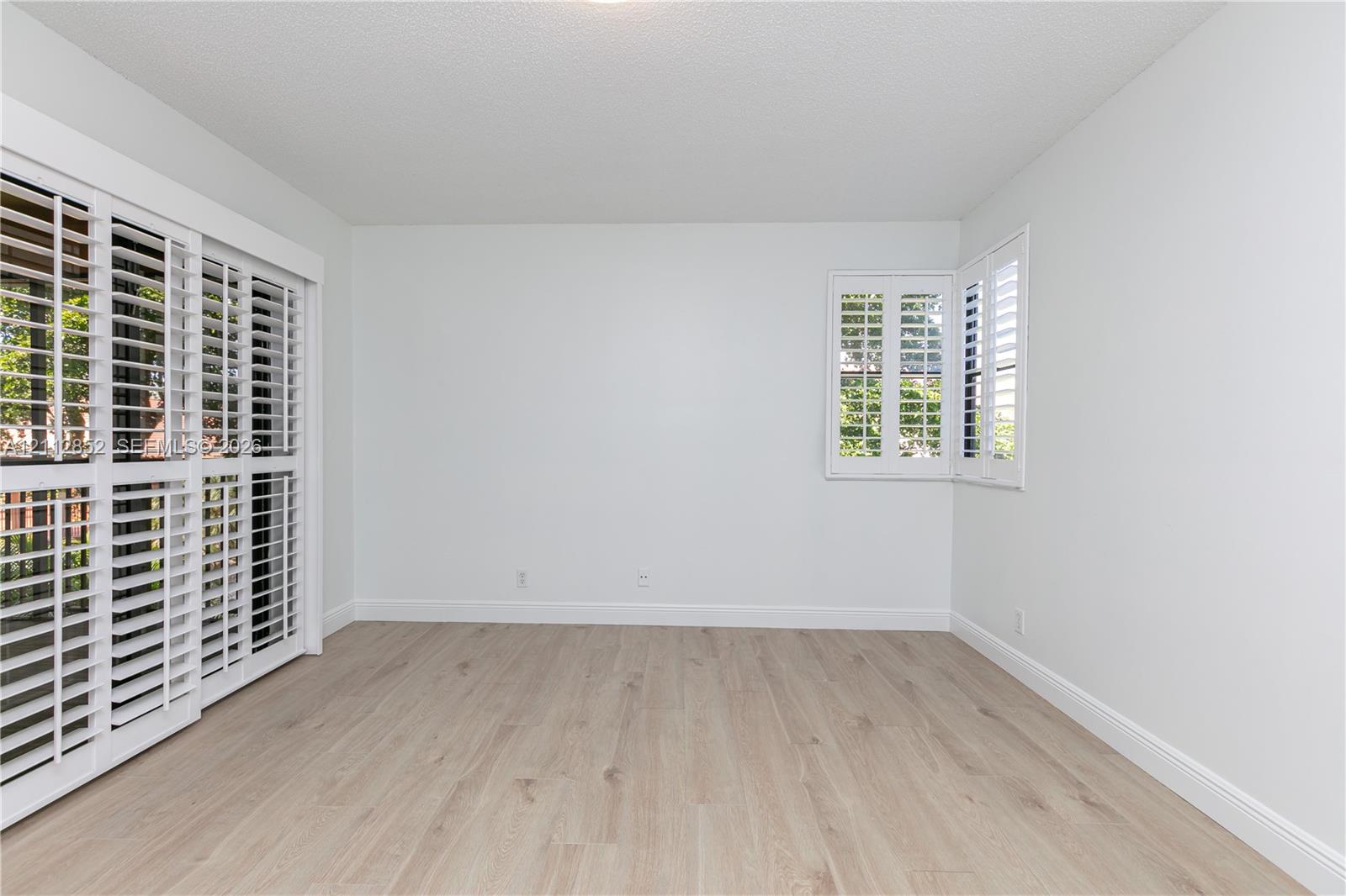 Neutral interior featuring wood-finish flooring, sliding glass doors, and white plantation shutters on windows