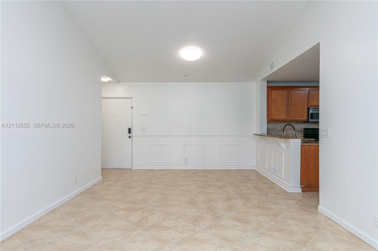 Interior space featuring ceramic tile flooring, wainscoting detail, vaulted ceiling, flush-mount lighting, and kitchen cabinetry with a breakfast bar