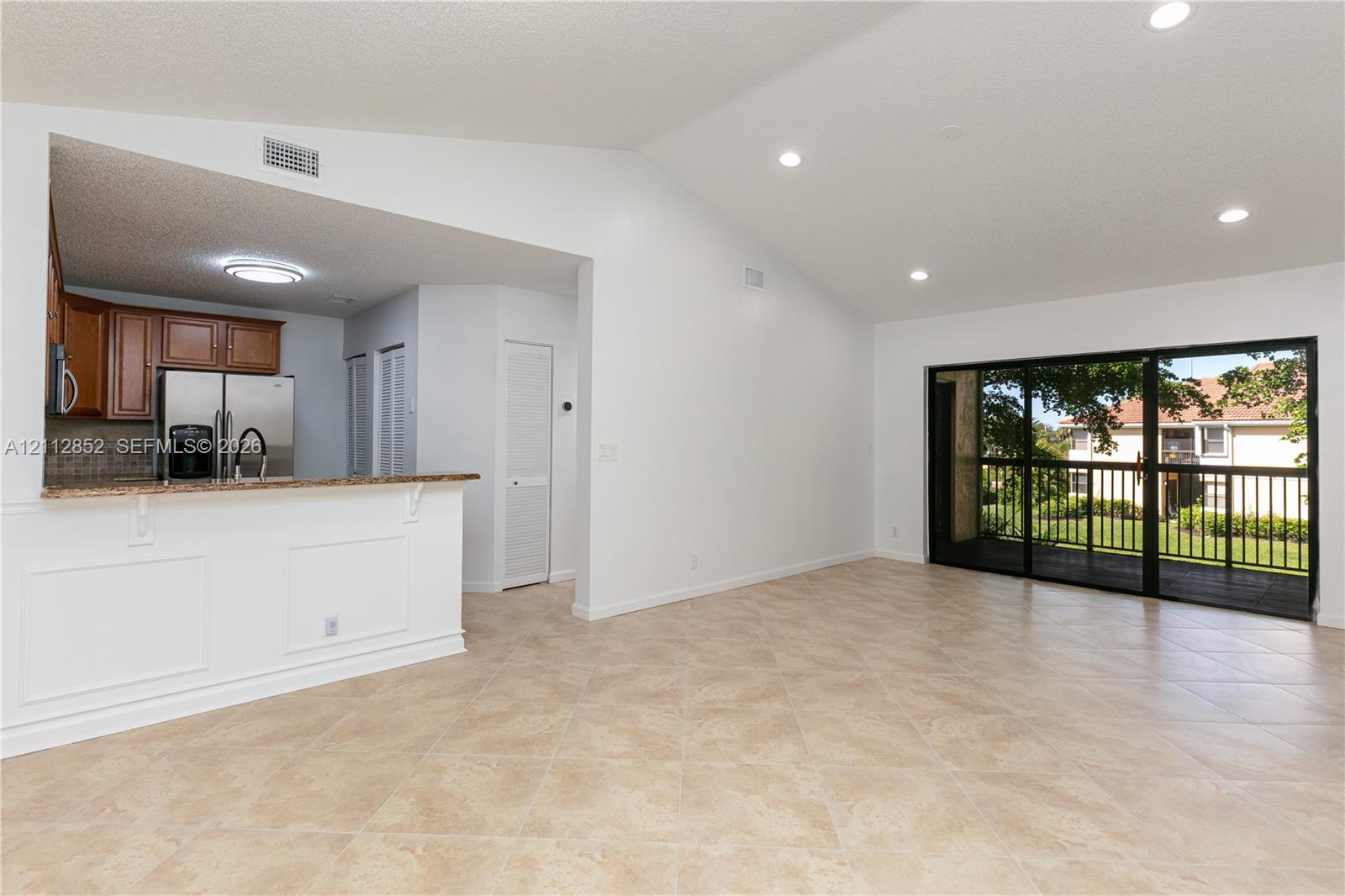 Vaulted ceilings, neutral tile flooring, recessed lighting, stone-surfaced breakfast bar, and large glass sliding doors providing exterior access