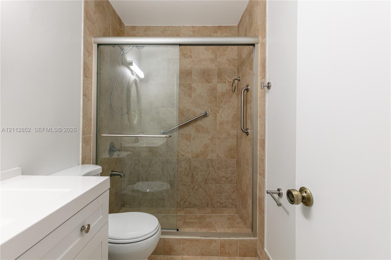 Walk-in shower featuring floor-to-ceiling tile surround, glass sliding door, integrated grab bars, and adjustable shower head