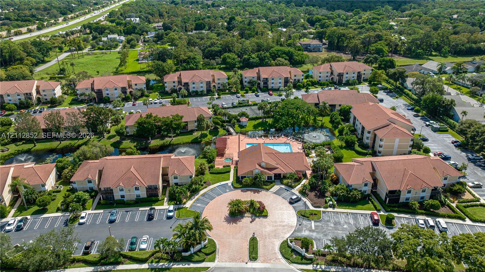 Multi-building residential complex featuring tile roofing, paved circular motor court, community swimming pool, and manicured landscaping