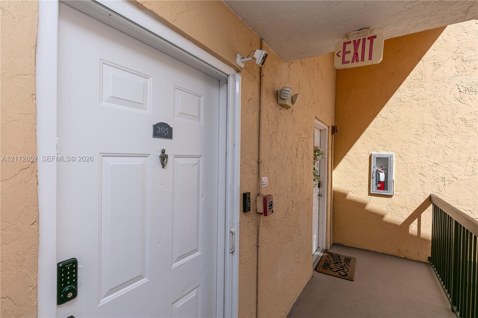 Exterior entrance featuring a white panel door, metal door knocker, digital keypad entry system, and a surveillance camera