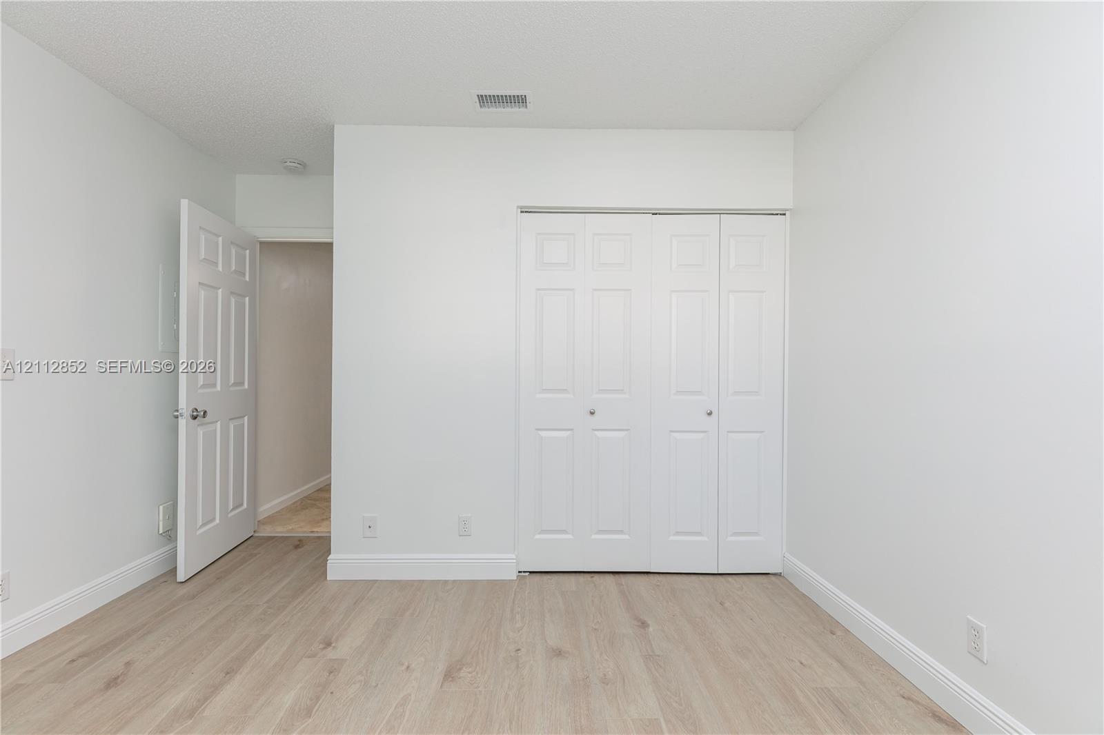 Room featuring neutral wall paint, wood-finish flooring, and a white bifold closet door