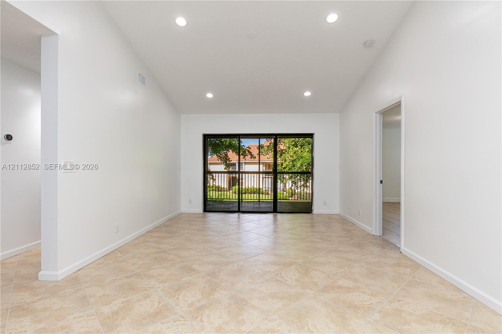 Vaulted ceilings, neutral tile flooring, recessed lighting, and large sliding glass doors featuring a black frame