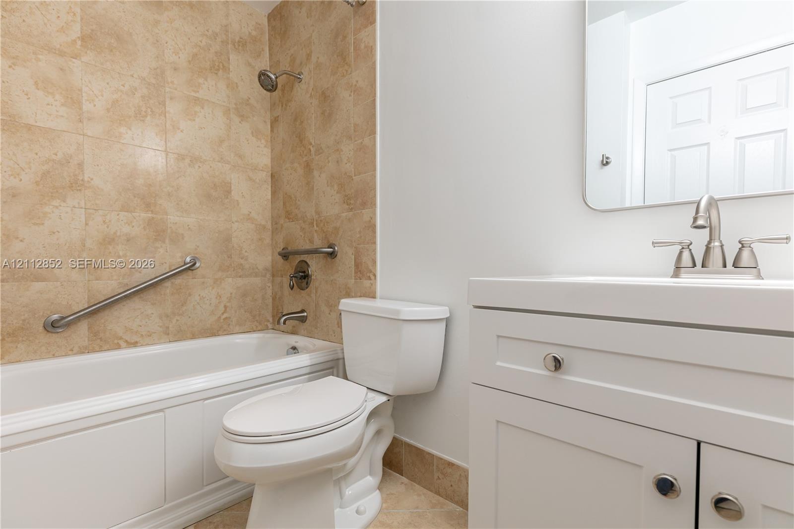 Bathroom featuring a white vanity cabinet with a integrated sink, polished metal faucet hardware, a tiled tub surround, and installed grab bars