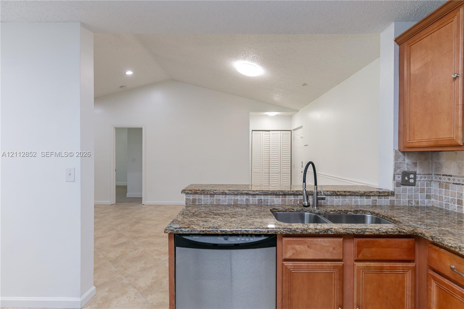 Kitchen featuring stone-finish countertops, tile backsplash, undermount double-basin sink, stainless steel dishwasher, and wooden cabinetry