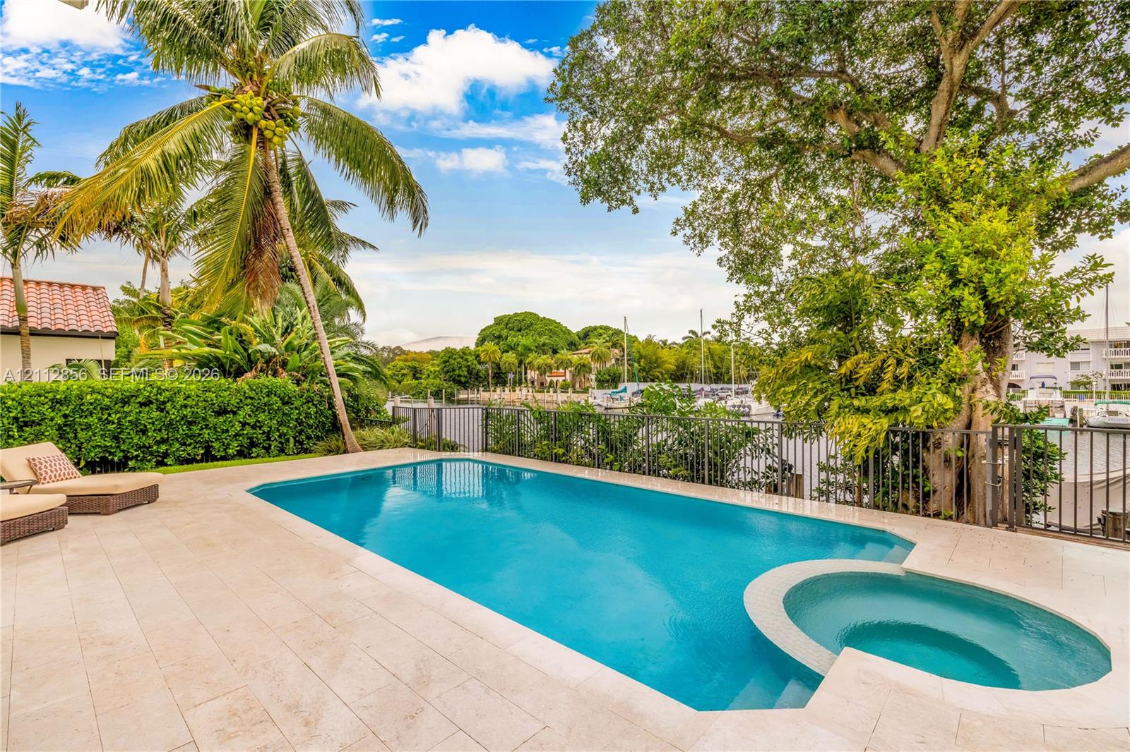 Outdoor pool featuring a built-in spa, paved stone patio, black metal fencing, and mature landscaping