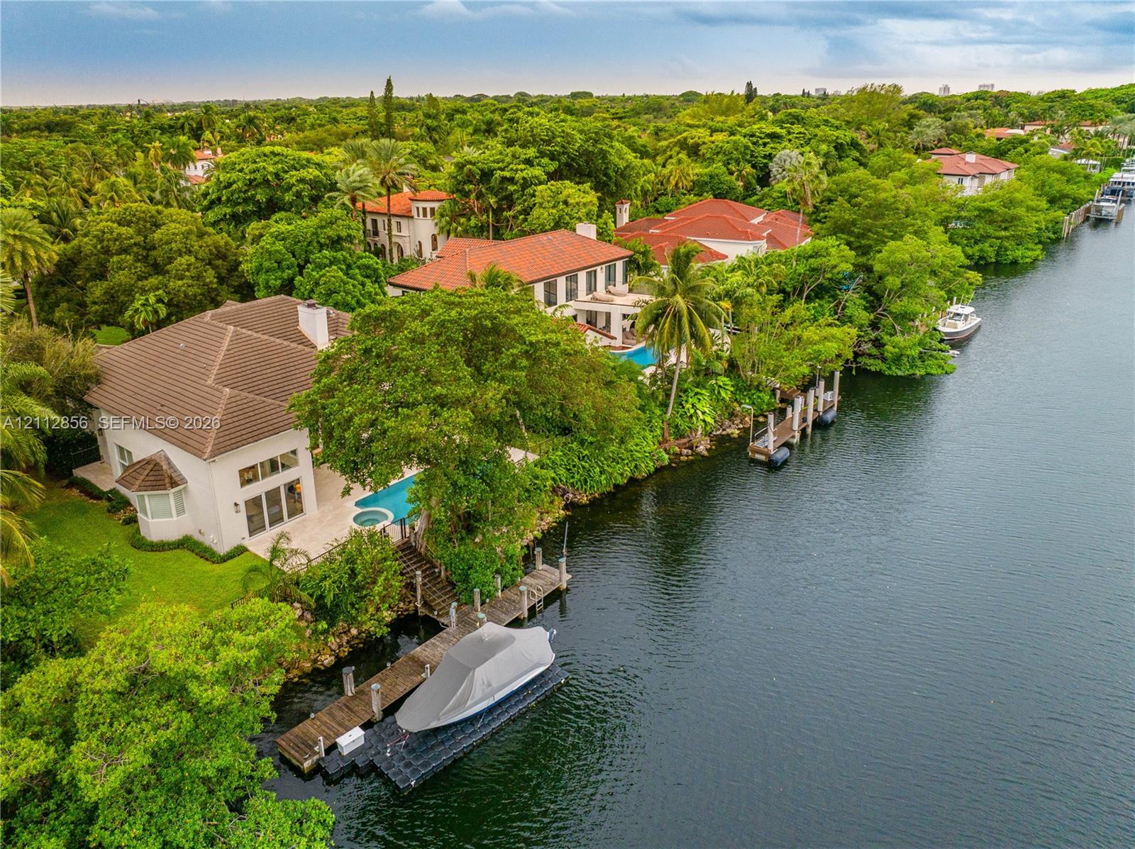 Waterfront estate featuring a private boat dock, tile roofing, an inground pool, and mature landscaping