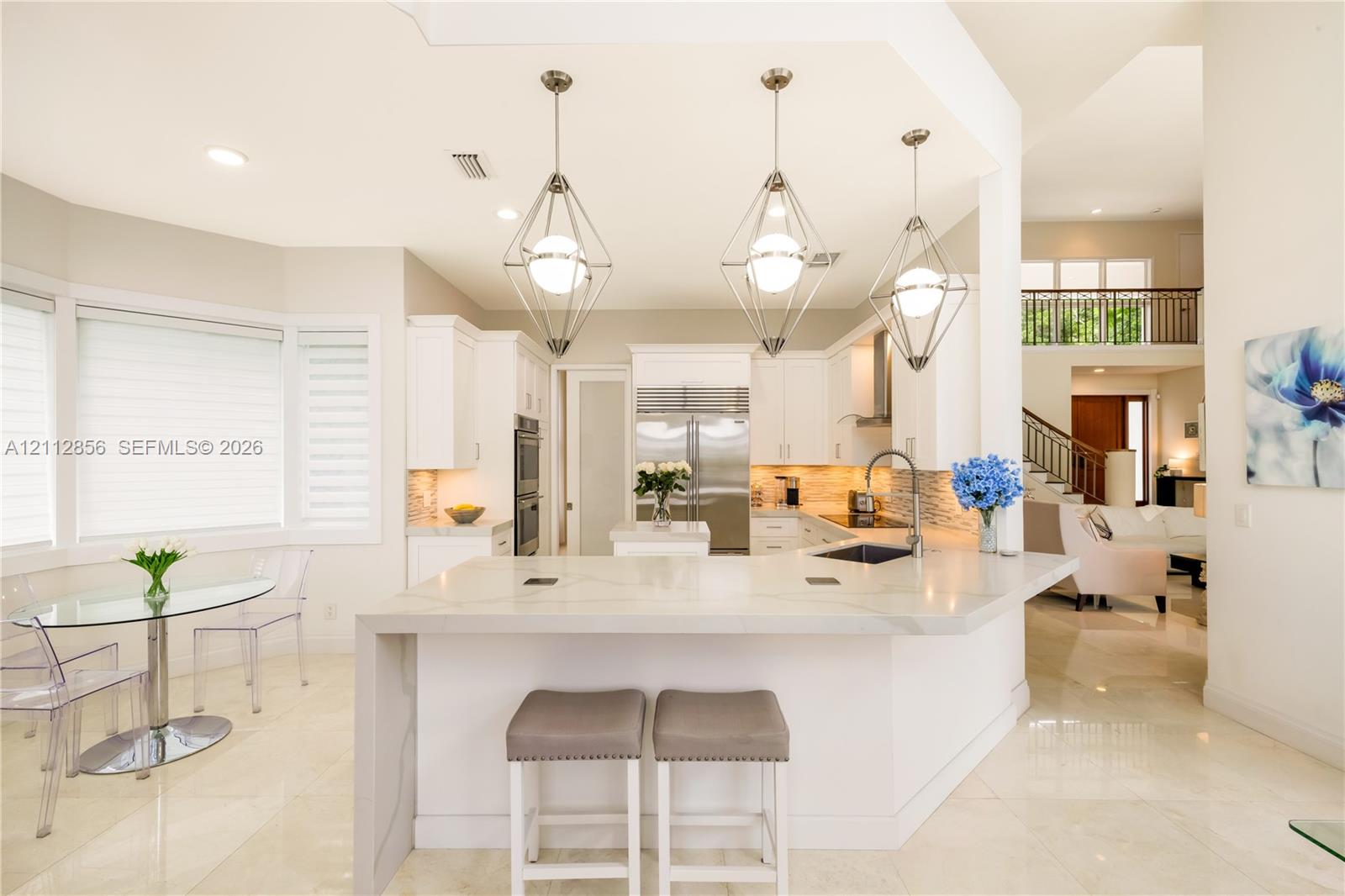 Kitchen featuring a waterfall-edge stone island, geometric pendant lighting, built-in double ovens, and professional-grade stainless steel refrigerator