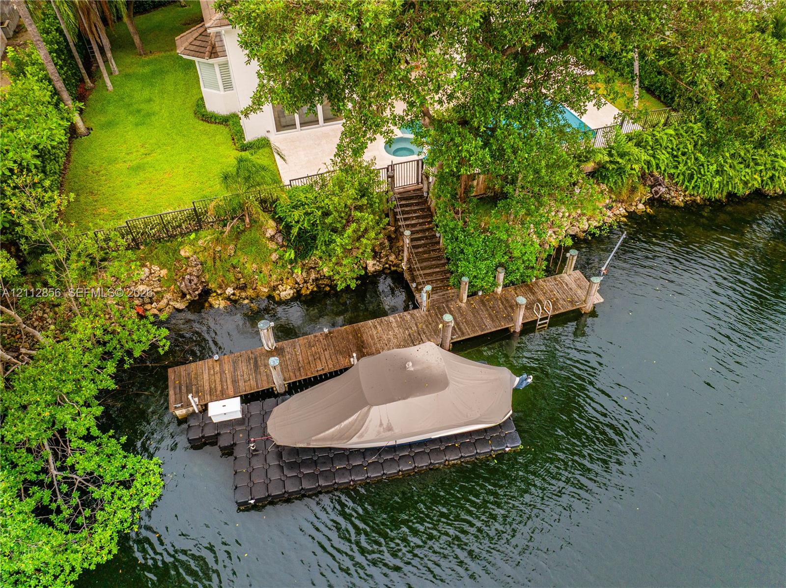 Waterfront property featuring a private wooden dock, modular floating boat lift, in-ground pool, integrated spa, and manicured landscaping