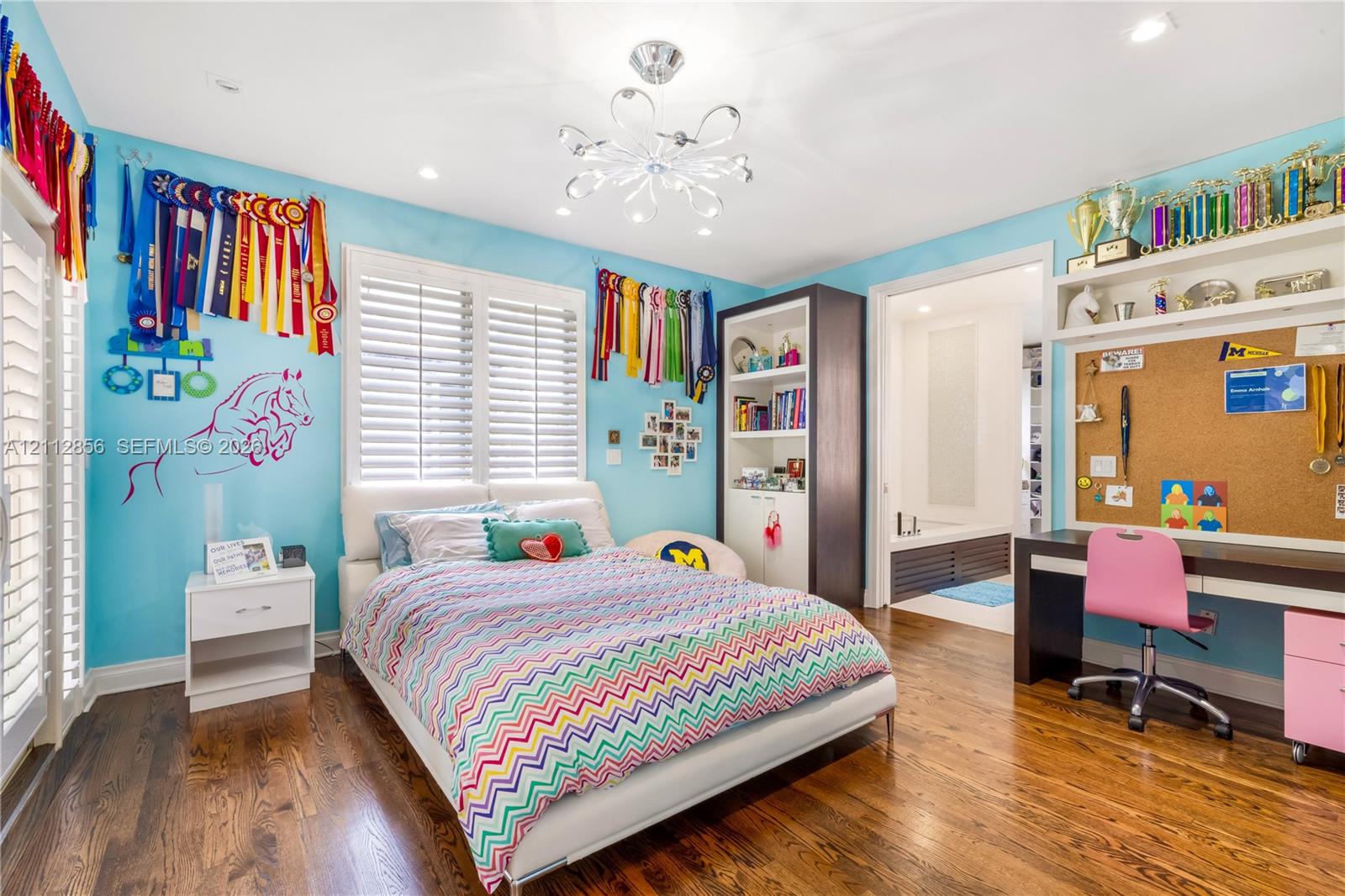 Hardwood flooring, multi-tier decorative ceiling light fixture, plantation shutters, built-in floor-to-ceiling cabinetry, and integrated desk with overhead shelving