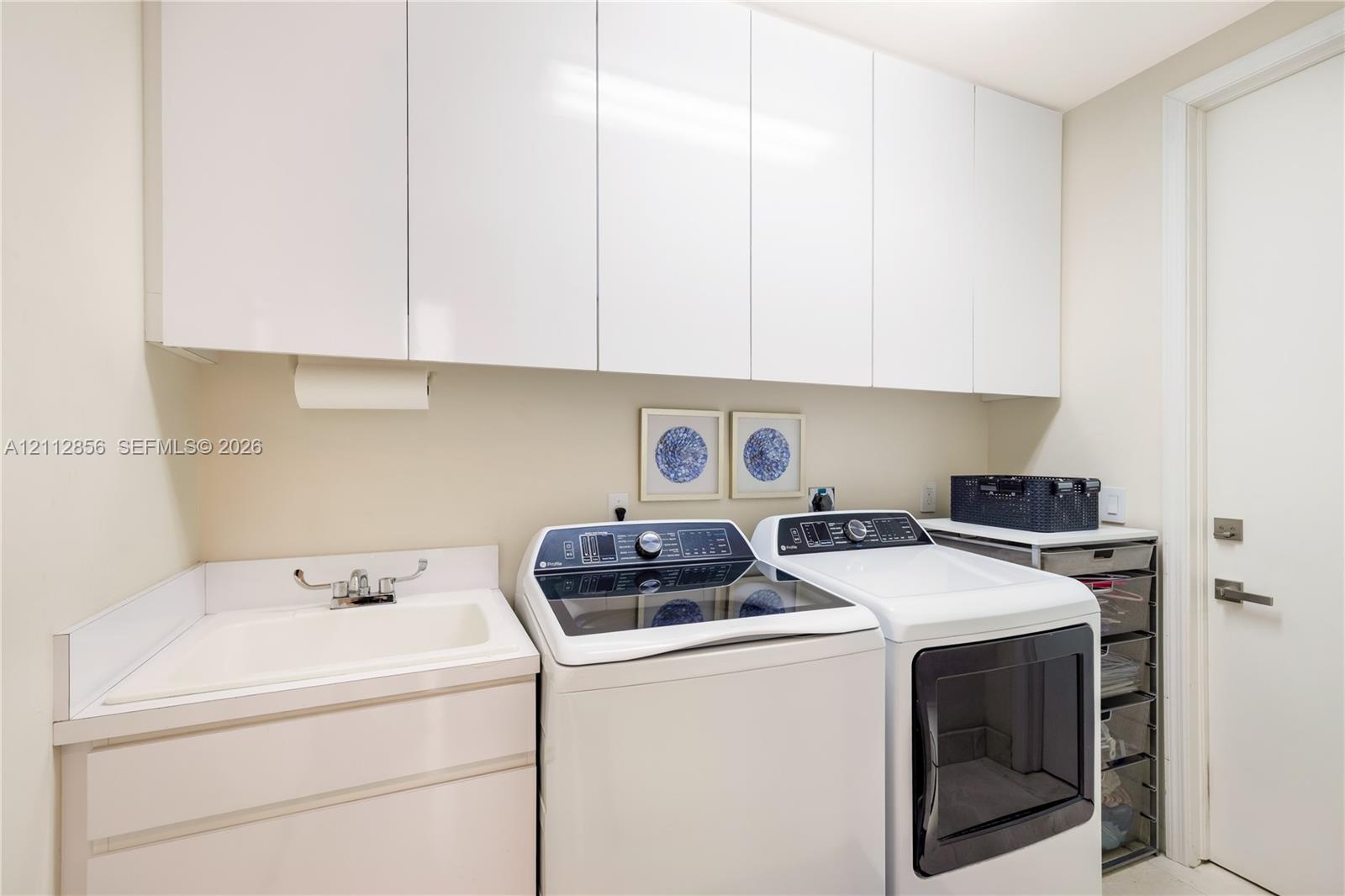 Laundry area featuring sleek white cabinetry, a built-in utility sink with a chrome faucet, and ample overhead storage