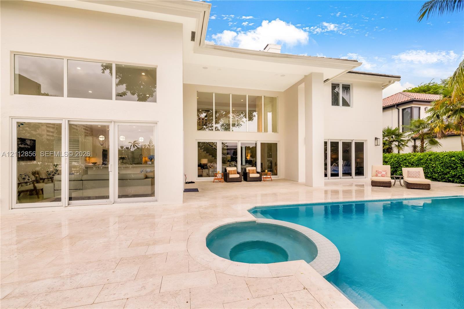 Exterior elevation featuring a stucco facade, expansive glass walls with multi-panel sliding doors, a stone-paved patio, and a swimming pool with a built-in spa