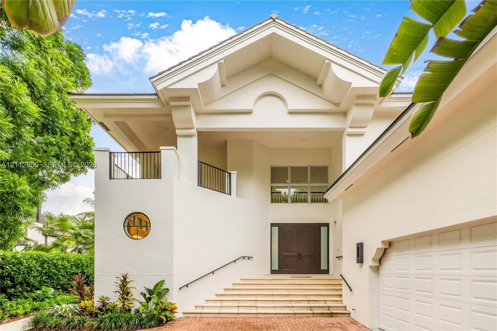 Architectural exterior featuring a vaulted gabled roofline, decorative corbels, a private second-story balcony with metal railings, a circular accent window, and double-entry doors