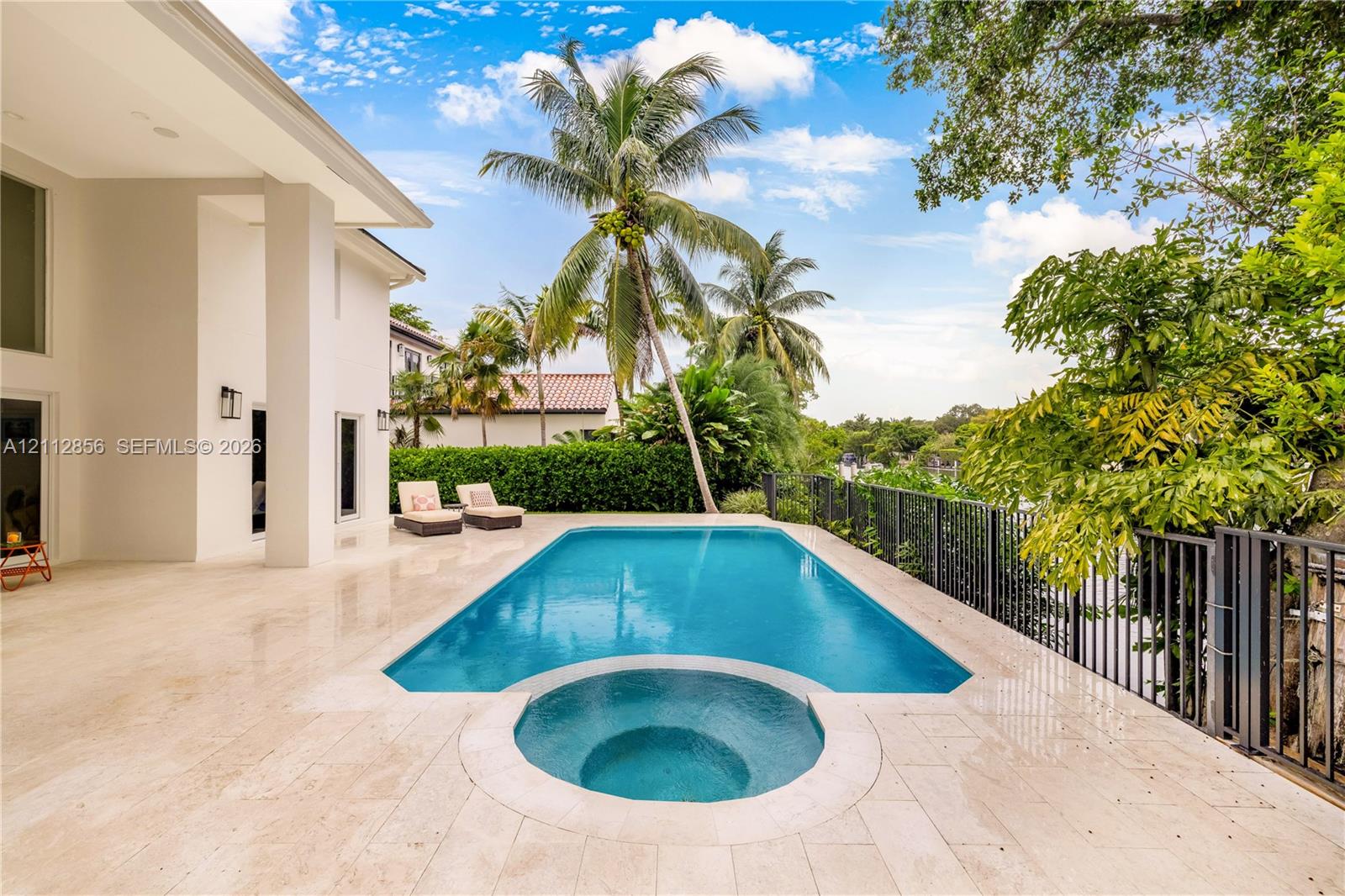Outdoor living space featuring a tiled pool deck, a swimming pool with an integrated spa, and metal perimeter fencing