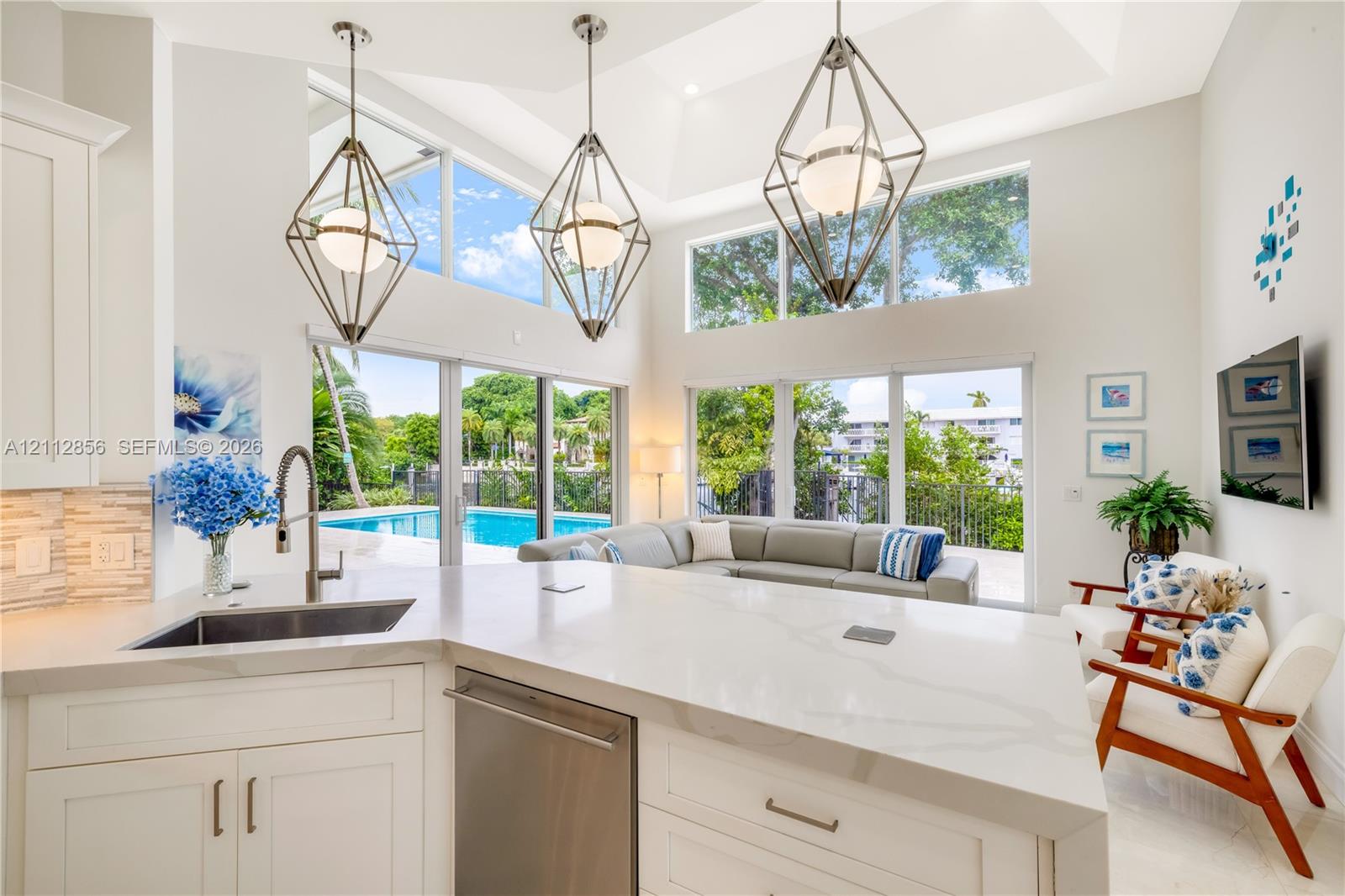 Kitchen island featuring a quartz countertop and stainless steel under-mount sink, high ceilings, geometric metal pendant lighting, and floor-to-ceiling glass panel doors