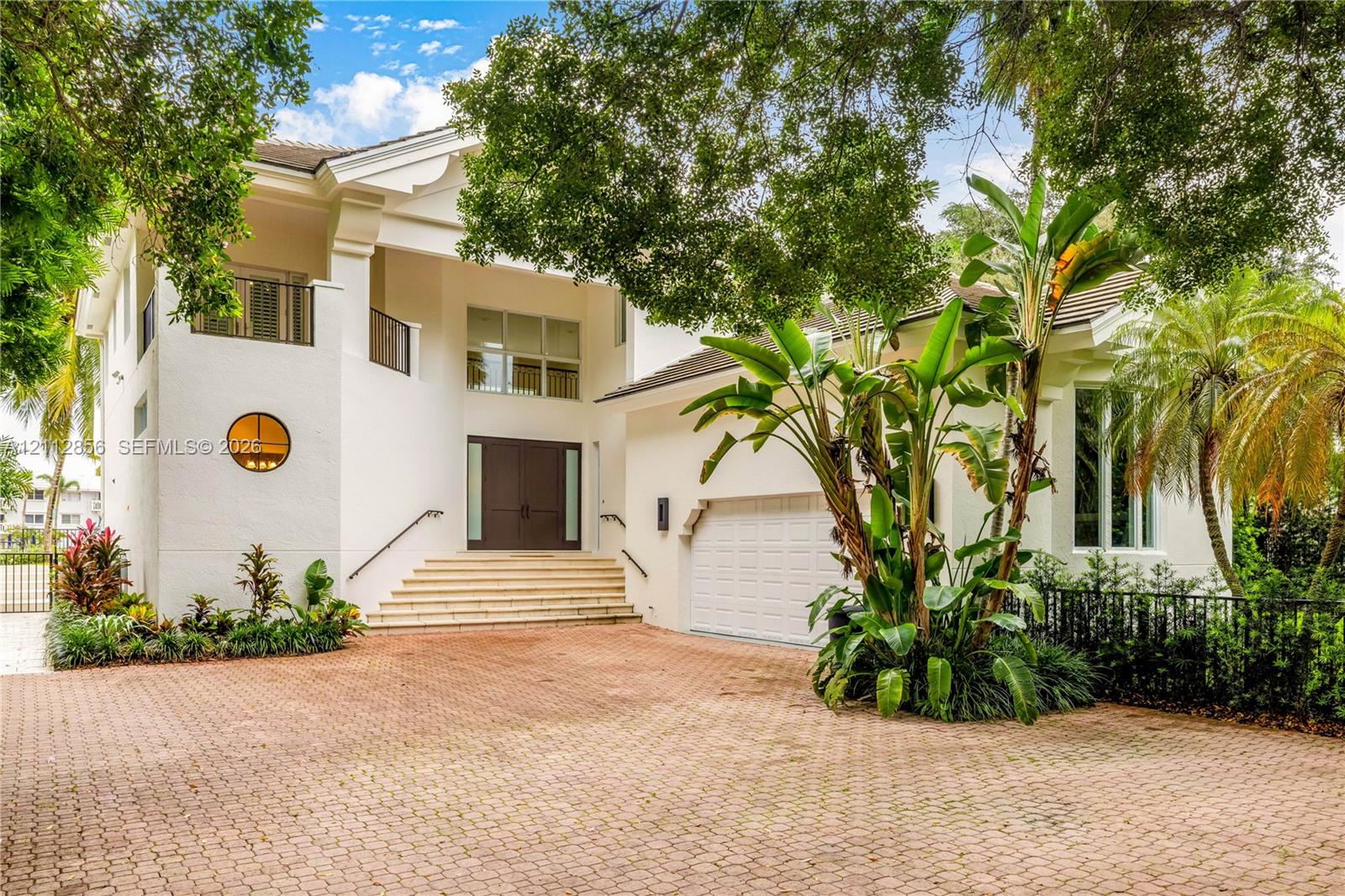 Two-story exterior featuring a paver driveway, double front doors, an elevated entryway with stone steps, a circular accent window, and a built-in garage