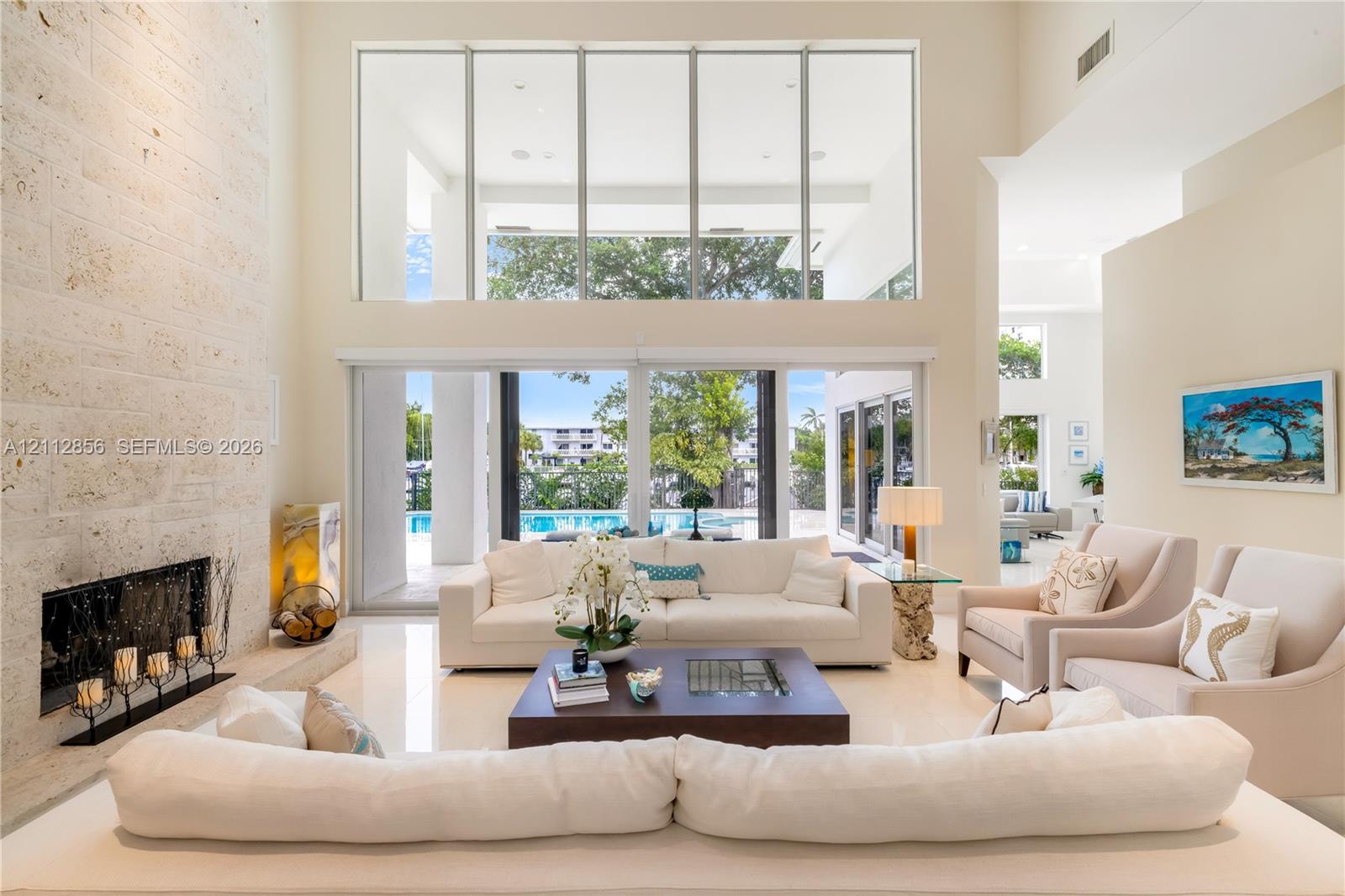 Double-height living area featuring floor-to-ceiling windows, a full-height stone-clad fireplace, polished tile flooring, and sliding glass doors
