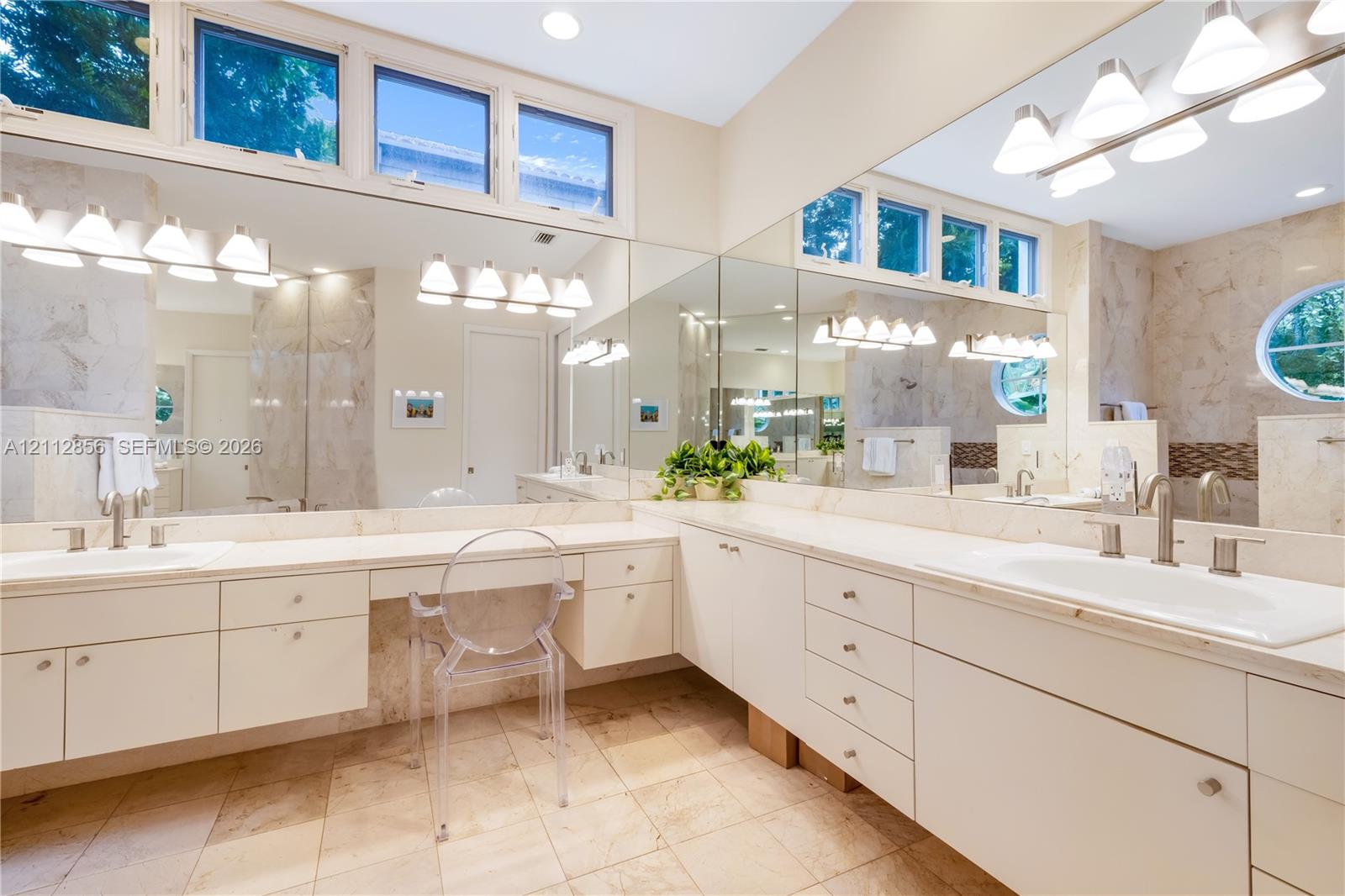 L-shaped vanity featuring a solid surface countertop, dual integrated sinks with brushed metal faucets, extensive built-in cabinetry, large-scale wall mirrors, and transom windows