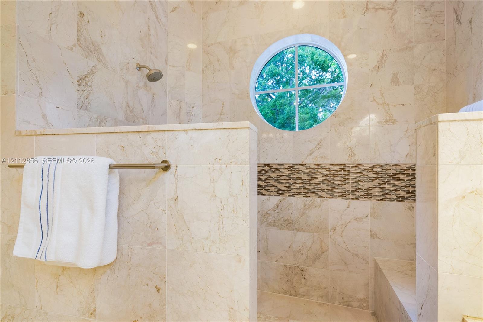 Walk-in shower featuring floor-to-ceiling stone tile, circular accent window, horizontal decorative stone inlay, built-in tiled bench, and wall-mounted shower head