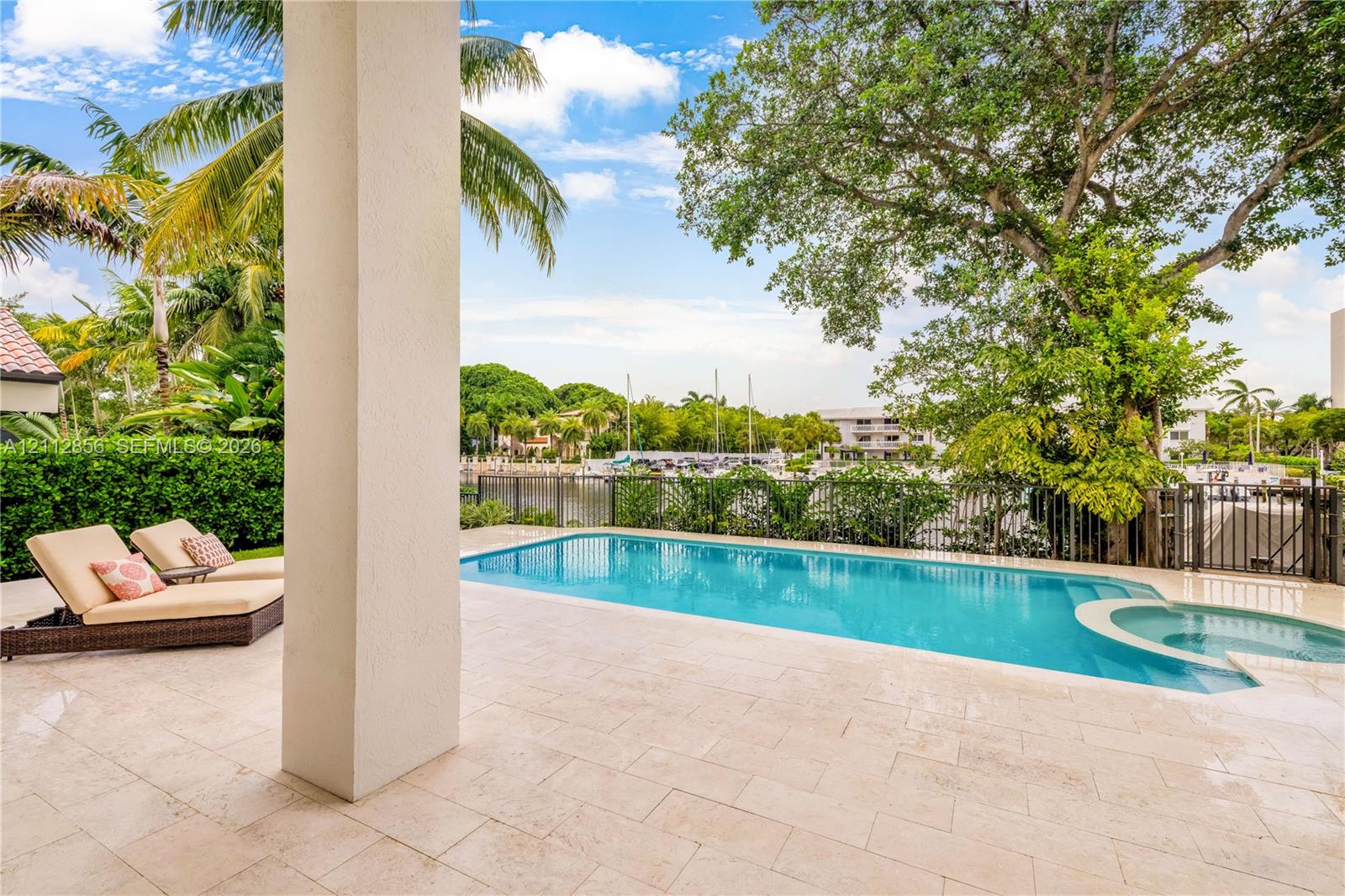 Covered patio with natural stone flooring, swimming pool with integrated spa, and metal perimeter fencing
