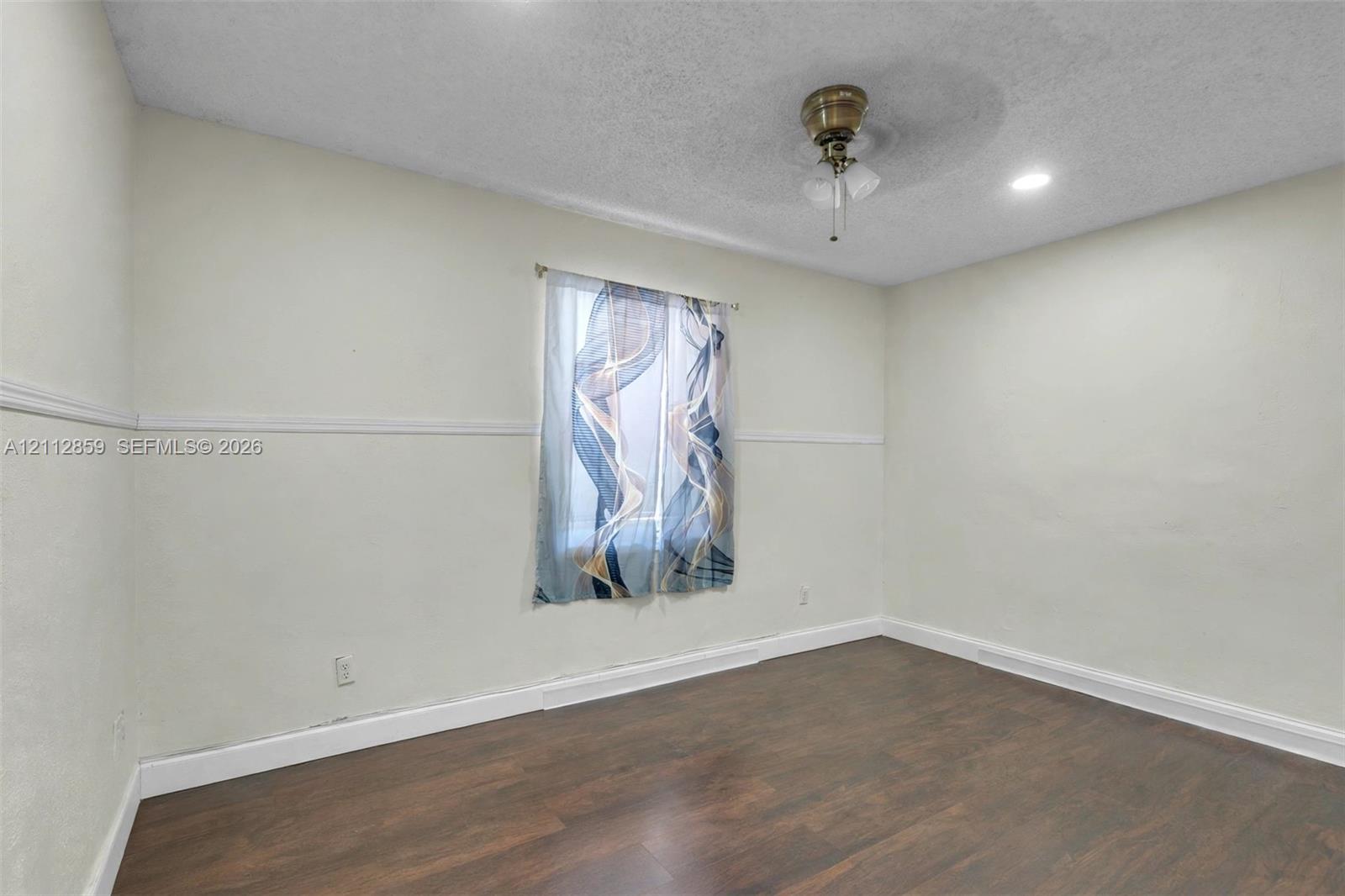 Interior space featuring dark wood-finish flooring, neutral walls with chair rail molding, a central ceiling fan with integrated lighting, and a single window