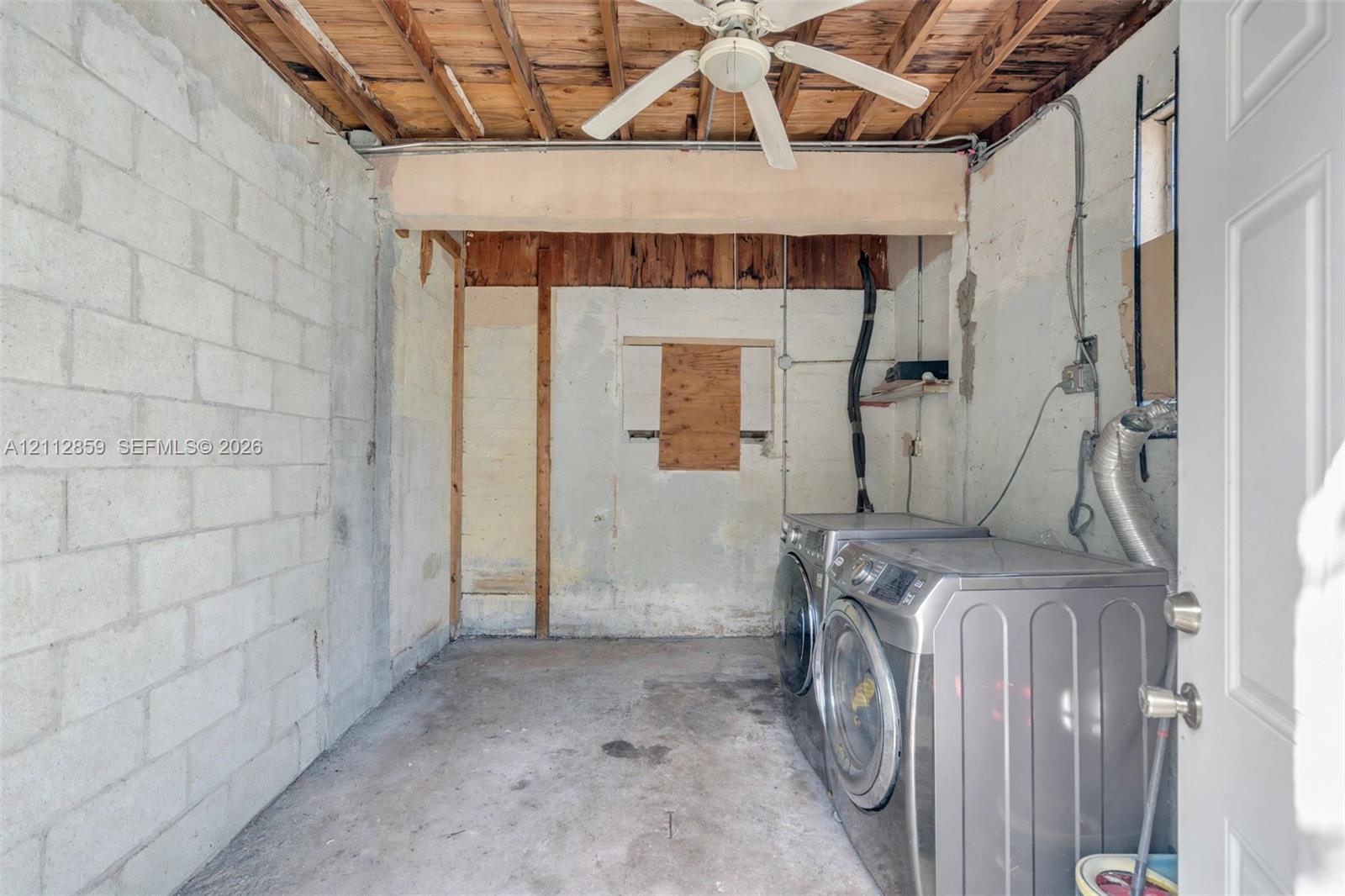 Utility space with exposed wood joist ceiling, concrete block walls, concrete flooring, and ceiling-mounted fan