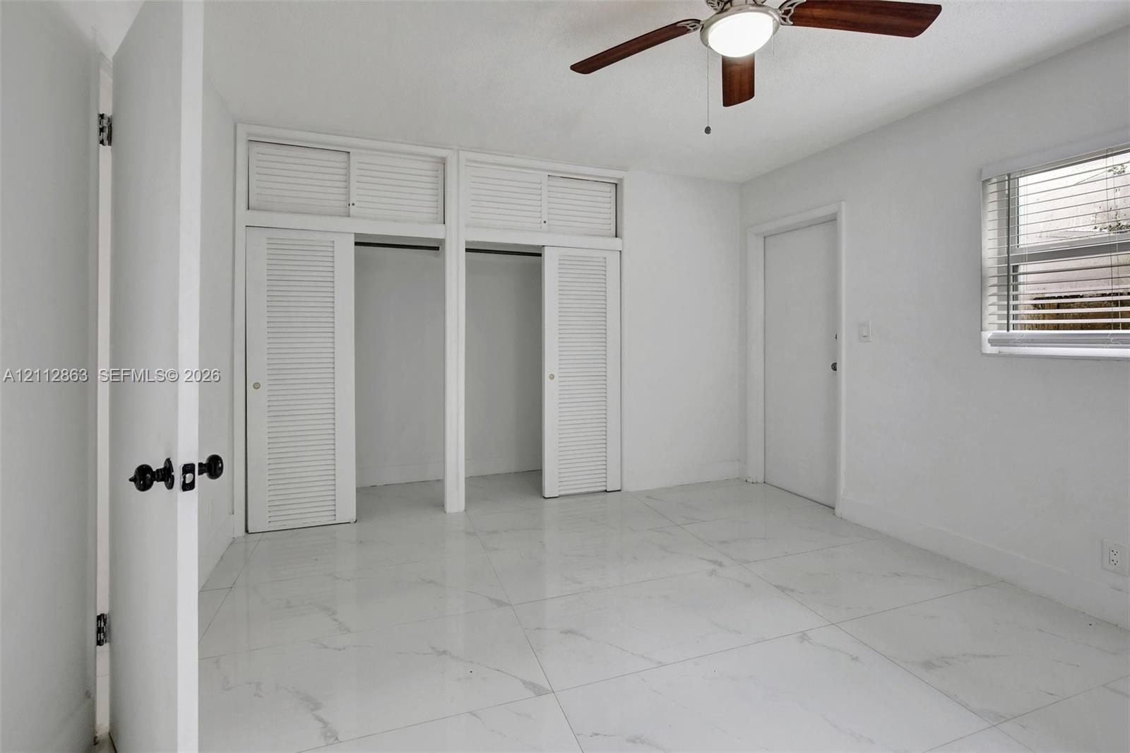 Large-format tile flooring, dual closets with overhead storage, and ceiling fan with integrated lighting
