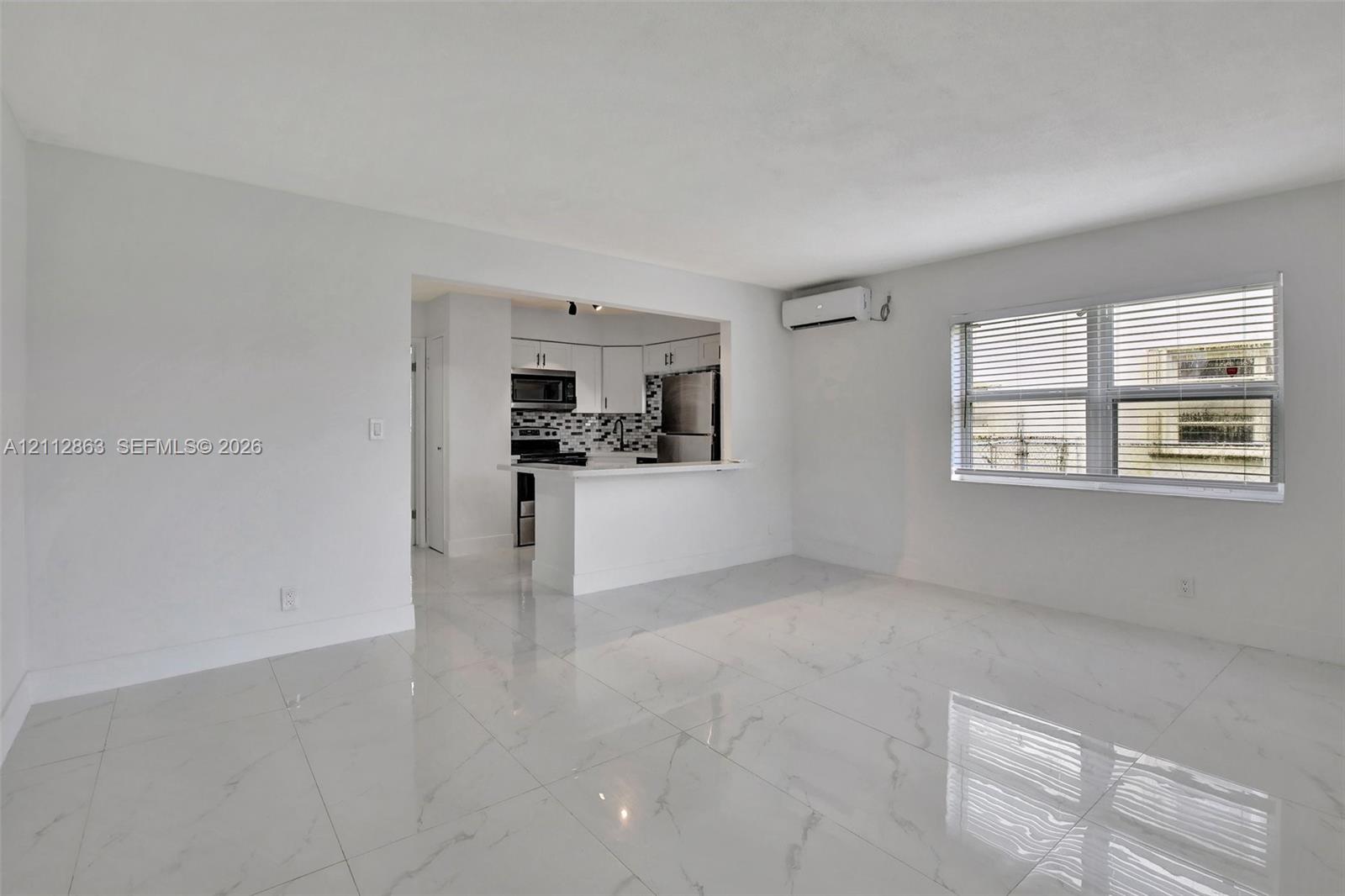 Polished stone-finish tile flooring, kitchen pass-through with breakfast bar, stainless steel appliances, patterned backsplash, and wall-mounted ductless climate control system