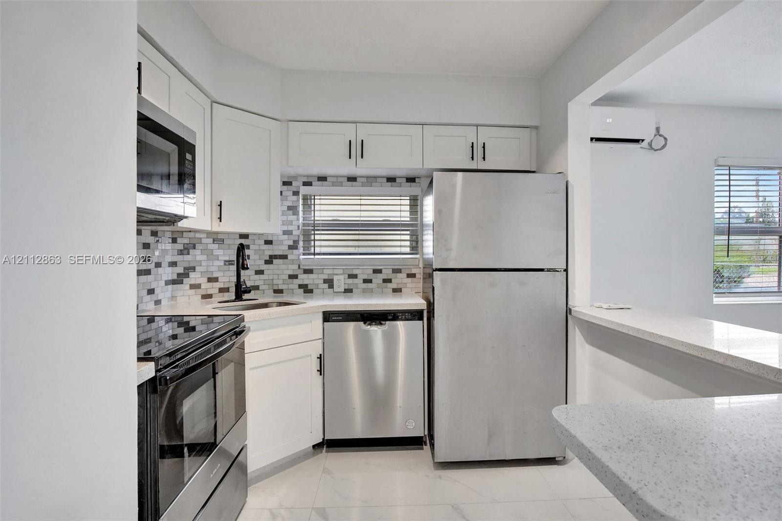 Kitchen featuring white Shaker-style cabinetry, stainless steel appliances, multi-toned mosaic tile backsplash, solid-surface countertops, and tile flooring
