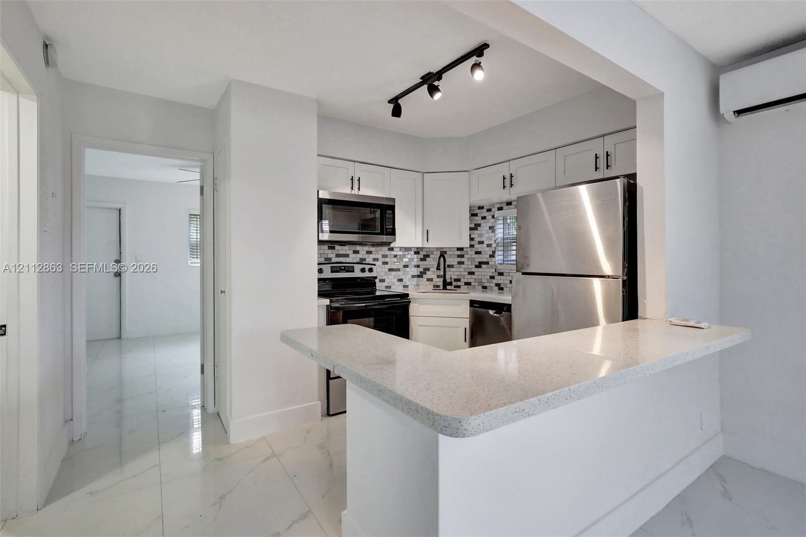 Kitchen featuring white cabinetry, quartz countertops with a breakfast bar, stone-tile backsplash, stainless steel appliances, and track lighting