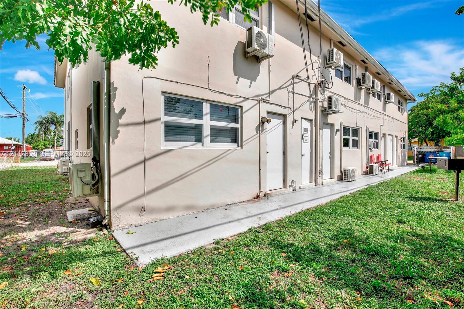 Stucco exterior building featuring multiple wall-mounted air conditioning units, sliding windows, and a poured concrete walkway