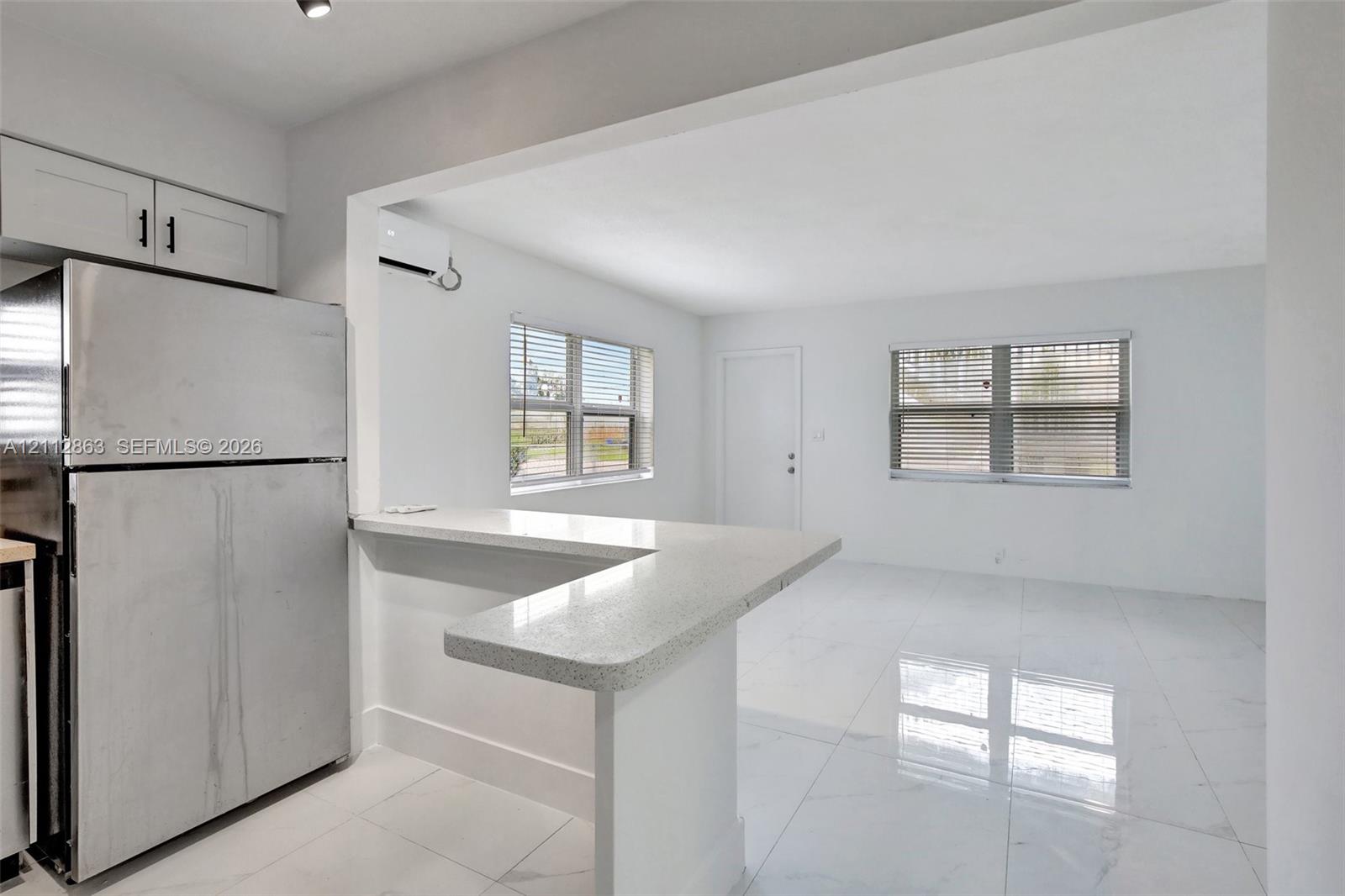 Kitchen featuring an L-shaped breakfast bar with quartz countertop, high-gloss tile flooring, stainless steel refrigerator, and white cabinetry
