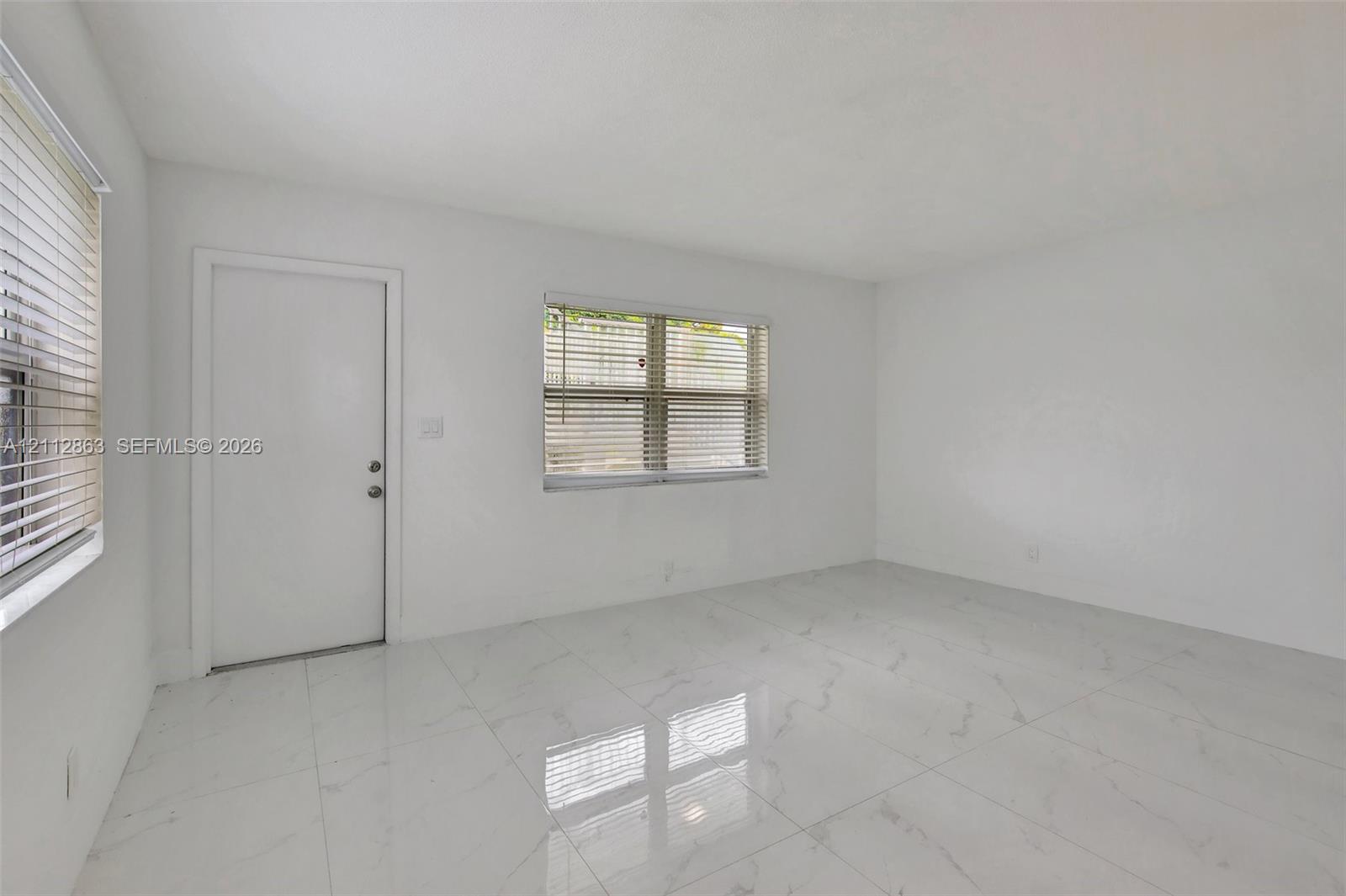 Neutral interior space featuring polished tile flooring, white wall finishes, and two windows with horizontal blinds