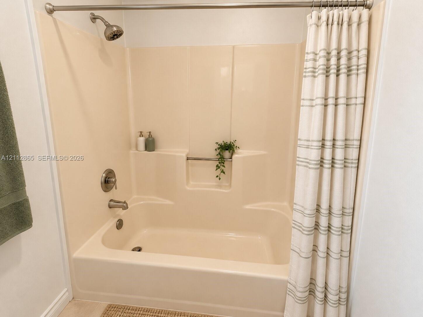 Bathtub and shower combination featuring a molded surround, integrated storage niche, and brushed nickel hardware