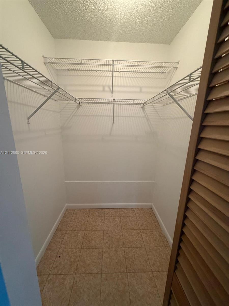 Walk-in closet featuring floor-to-ceiling white walls, ceramic tile flooring, and integrated white wire shelving