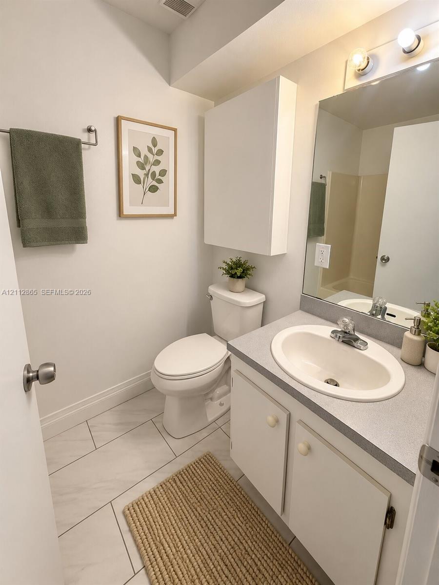 Bathroom featuring a vanity with a solid-surface countertop, an integrated oval sink, a wall-mounted storage cabinet, and large-format tile flooring
