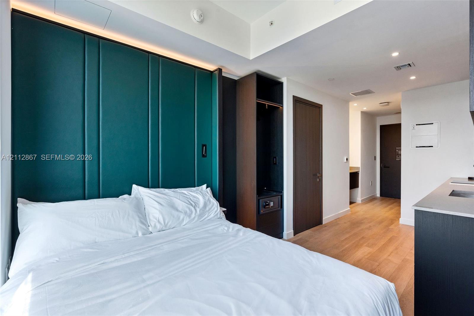 Deep teal paneled accent wall with integrated cove lighting, light wood-finish flooring, and dark wood-finish built-in cabinetry Deep teal paneled accent wall with integrated cove lighting, light wood-finish flooring, and dark wood-finish built-in cabinetry
