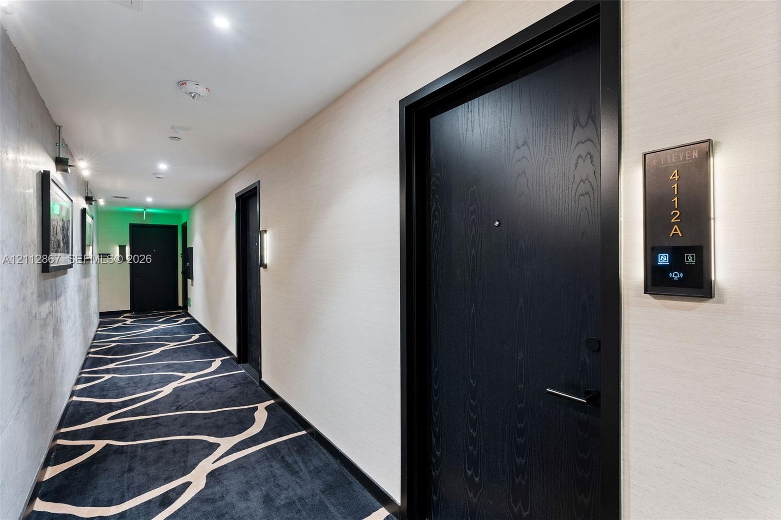 Hallway featuring textured wallpaper, patterned carpeting, recessed ceiling lighting, and matte black doors with electronic entry systems Hallway featuring textured wallpaper, patterned carpeting, recessed ceiling lighting, and matte black doors with electronic entry systems