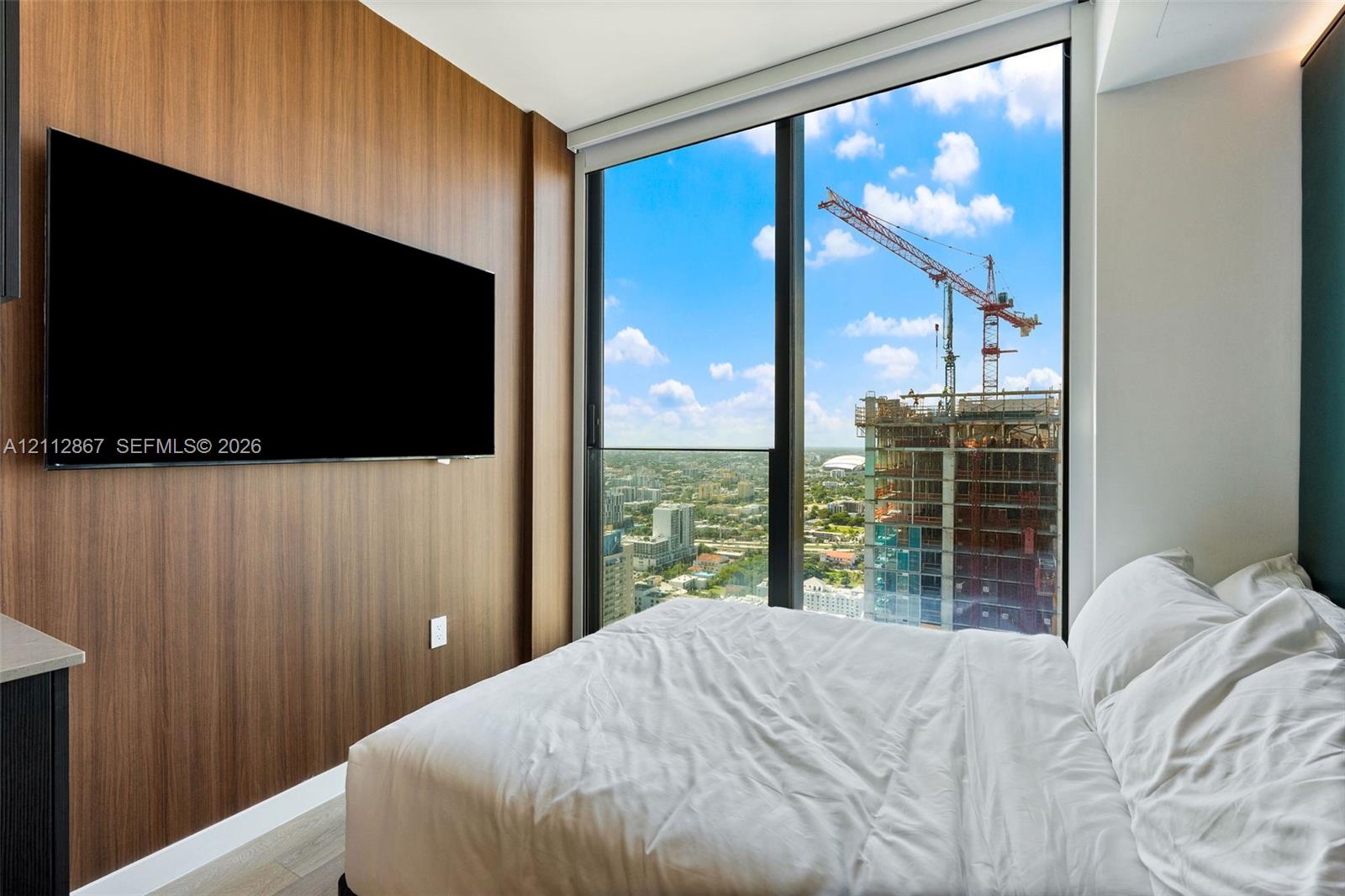 Floor-to-ceiling windows, wood-finish accent wall, and light-toned flooring Floor-to-ceiling windows, wood-finish accent wall, and light-toned flooring