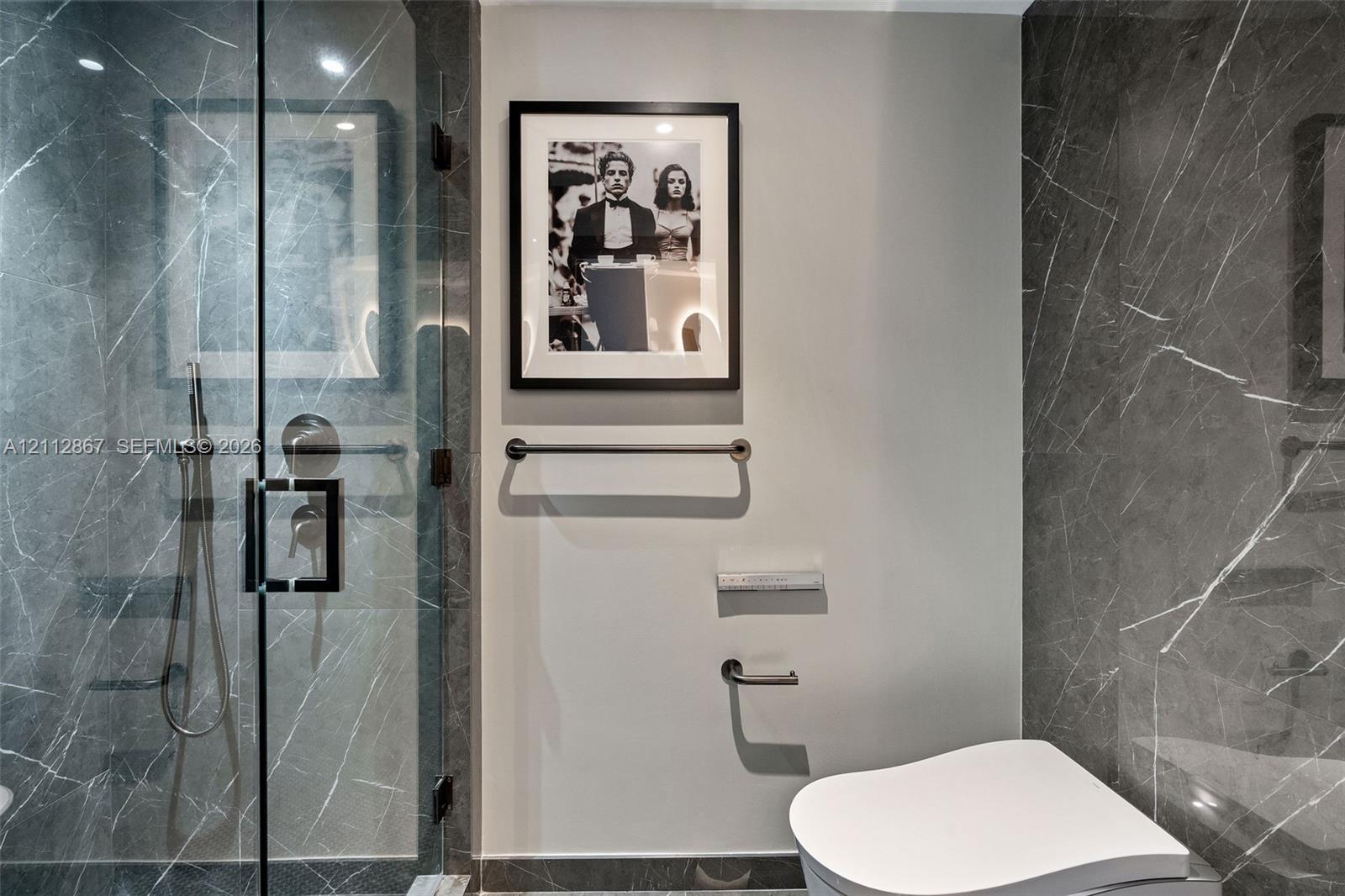 Shower stall featuring full-height stone-finish wall tile, a frameless glass door, and a handheld spray fixture, complemented by polished metal hardware and fixtures