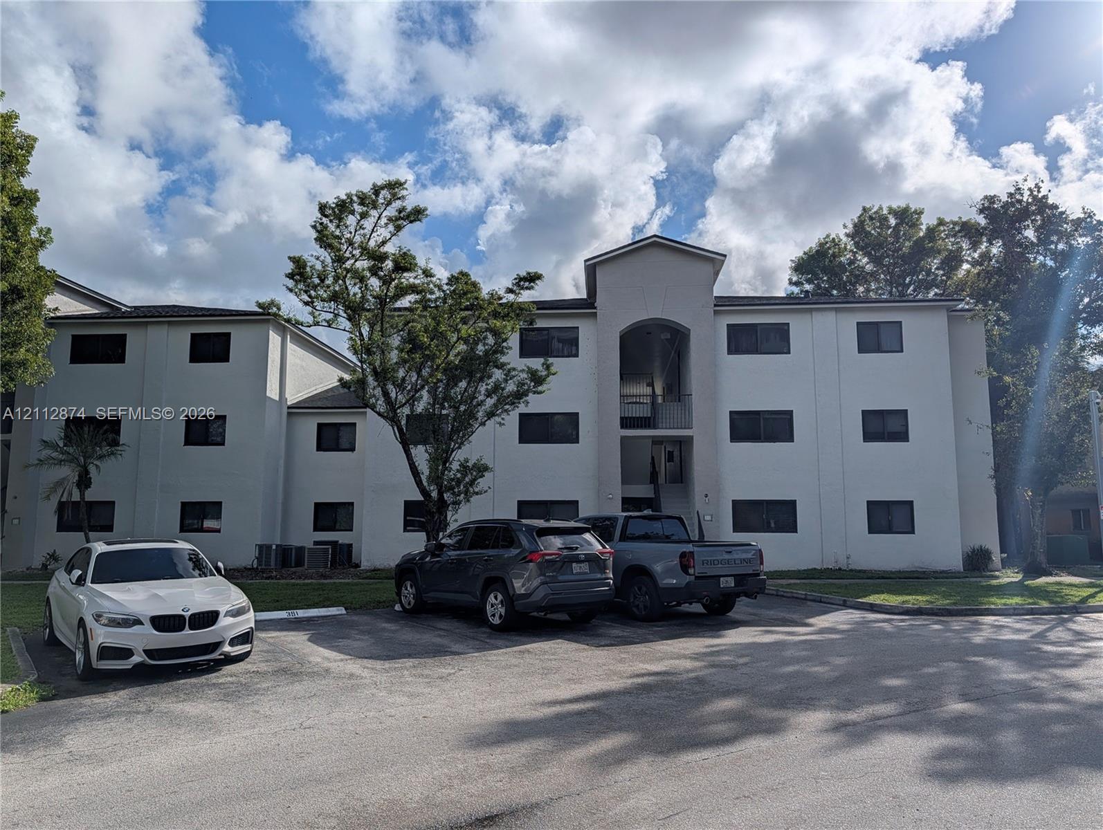 Multi-story residential building featuring a stucco exterior, arched entryway, and dedicated paved surface parking