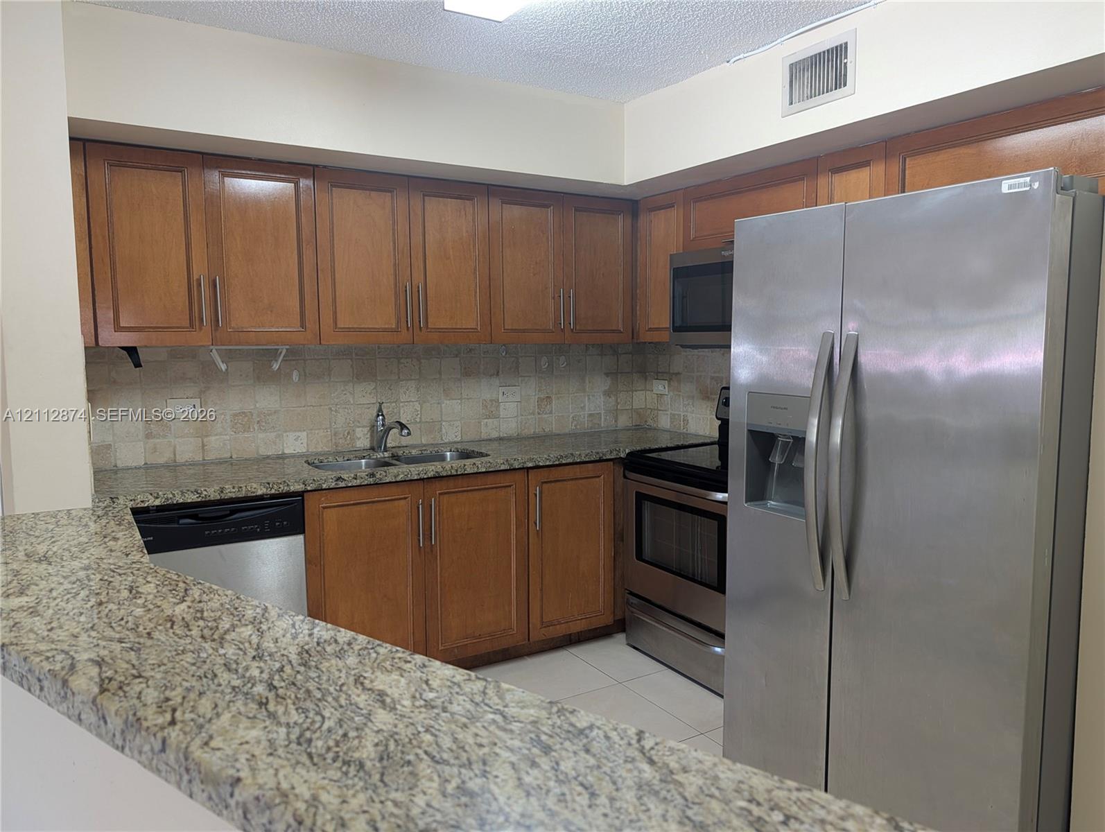 Kitchen featuring wood cabinetry, stone-surface countertops, stone tile backsplash, and stainless steel appliances
