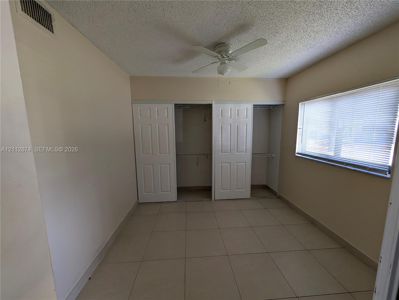 Room featuring neutral-toned tile flooring, dual-panel closet doors, and a ceiling-mounted fan