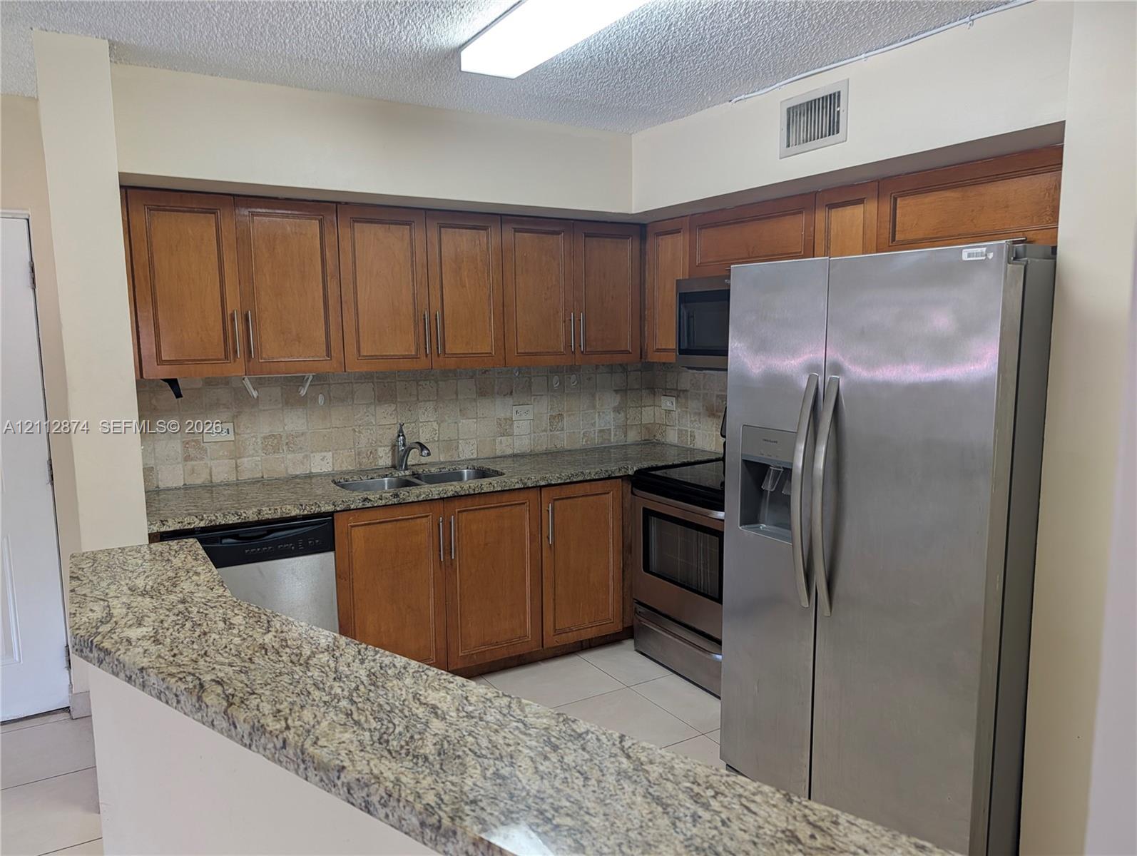 Kitchen featuring wood cabinetry, stone countertops, a tile backsplash, and stainless steel appliances