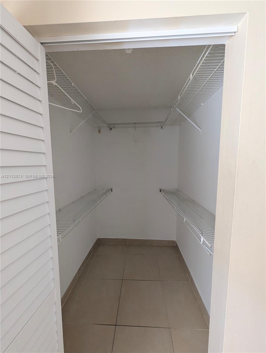 Storage closet featuring louvered bi-fold doors, white wire shelving, and large-format tile flooring