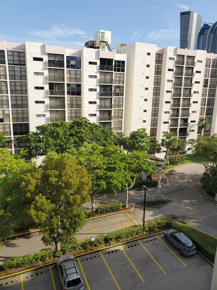 Multi-story residential building exterior featuring private balconies, expansive landscaped grounds with mature trees, and designated surface parking Multi-story residential building exterior featuring private balconies, expansive landscaped grounds with mature trees, and designated surface parking