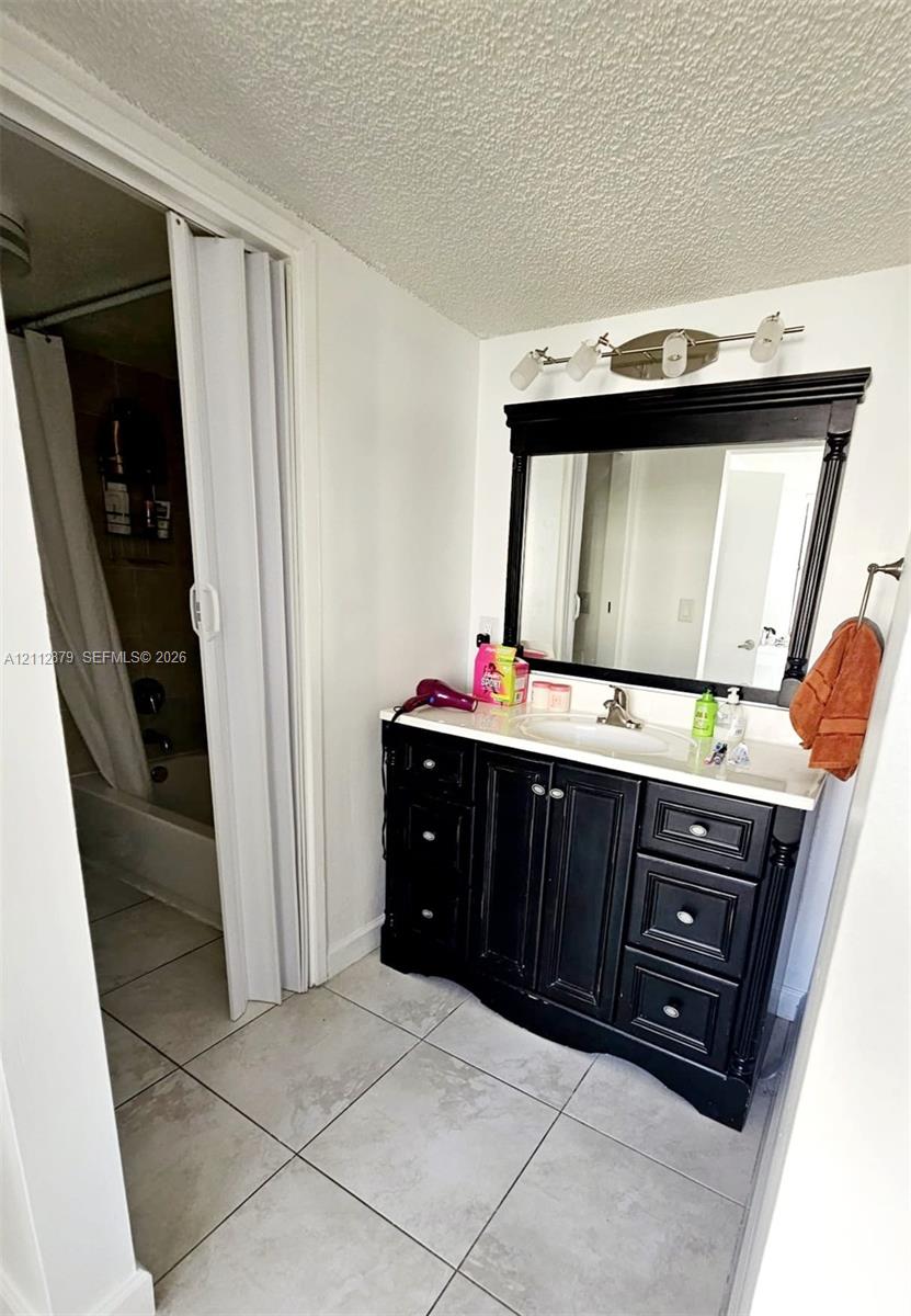 Vanity featuring a dark-toned finish, light-toned countertop with an integrated basin, matching framed mirror, multi-light fixture, and ceramic tile flooring