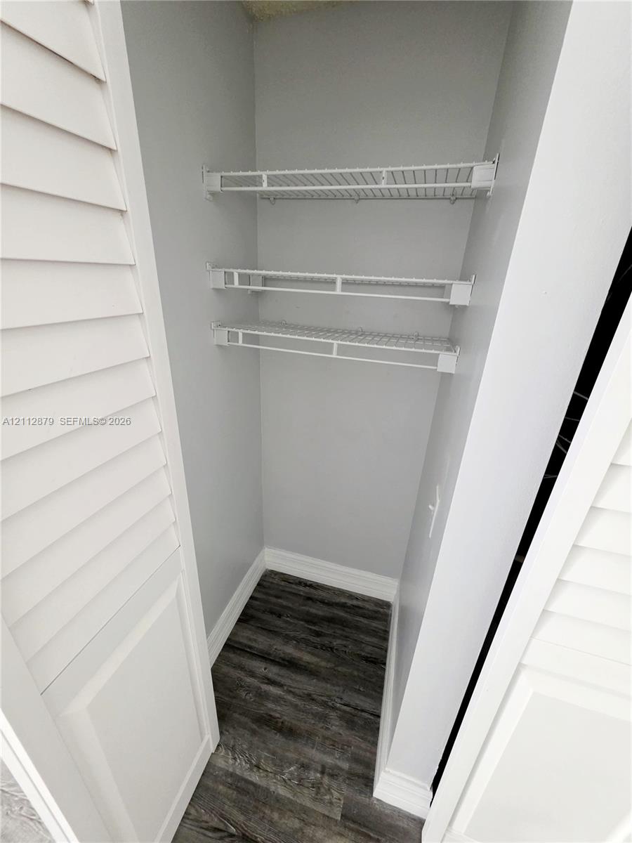 Storage space featuring louvered bi-fold doors, three tiers of white wire shelving, and wood-finish flooring