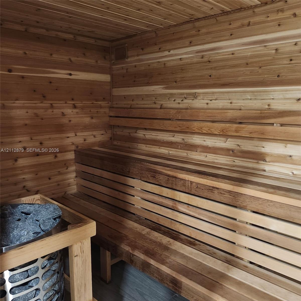 Sauna featuring tongue-and-groove wood paneling, multi-level built-in bench seating, and a dedicated stone-filled heater unit Sauna featuring tongue-and-groove wood paneling, multi-level built-in bench seating, and a dedicated stone-filled heater unit